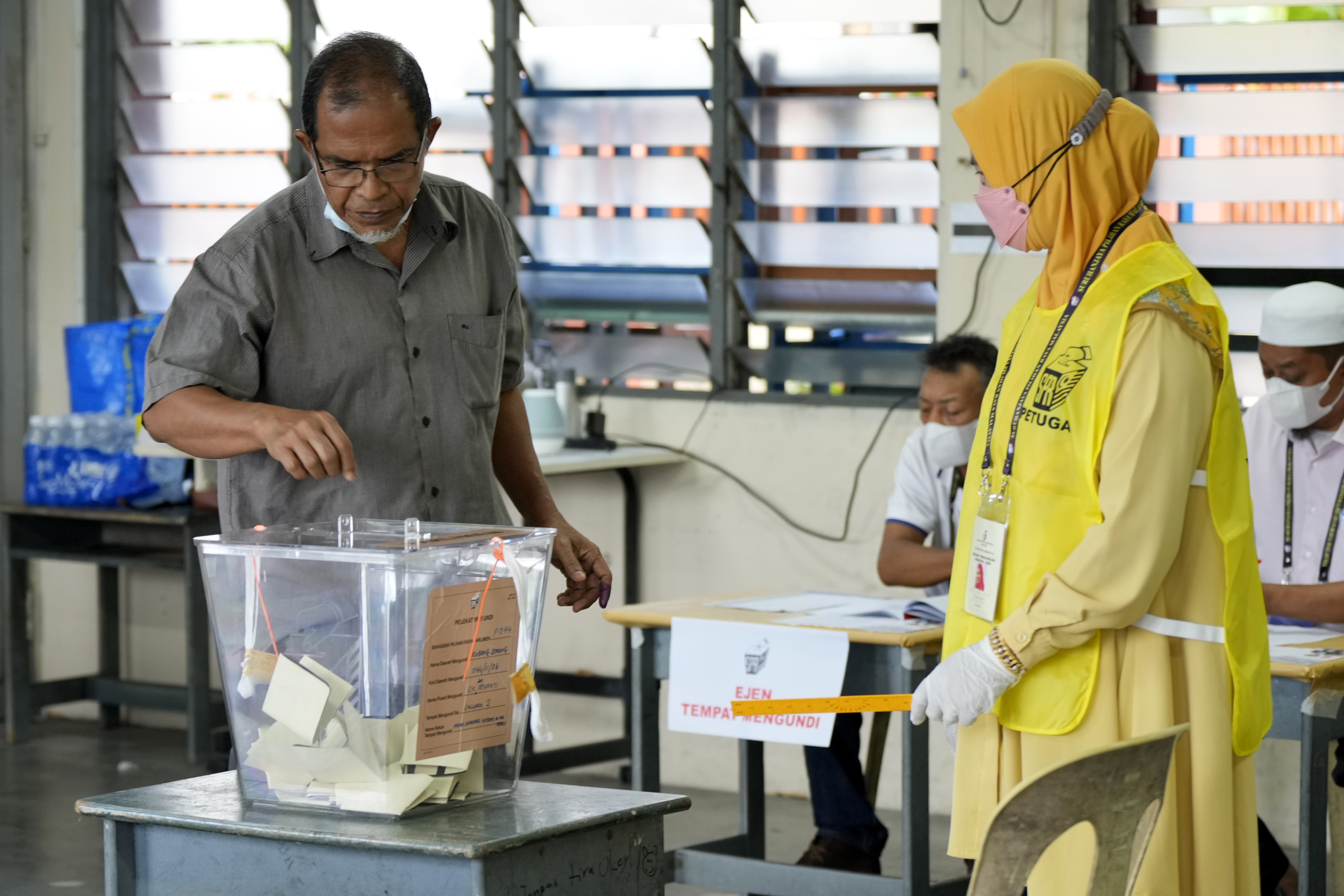 A voter puts his ballot in the box in a polling station set up in a classroom as an alection officials wearing yellow watches