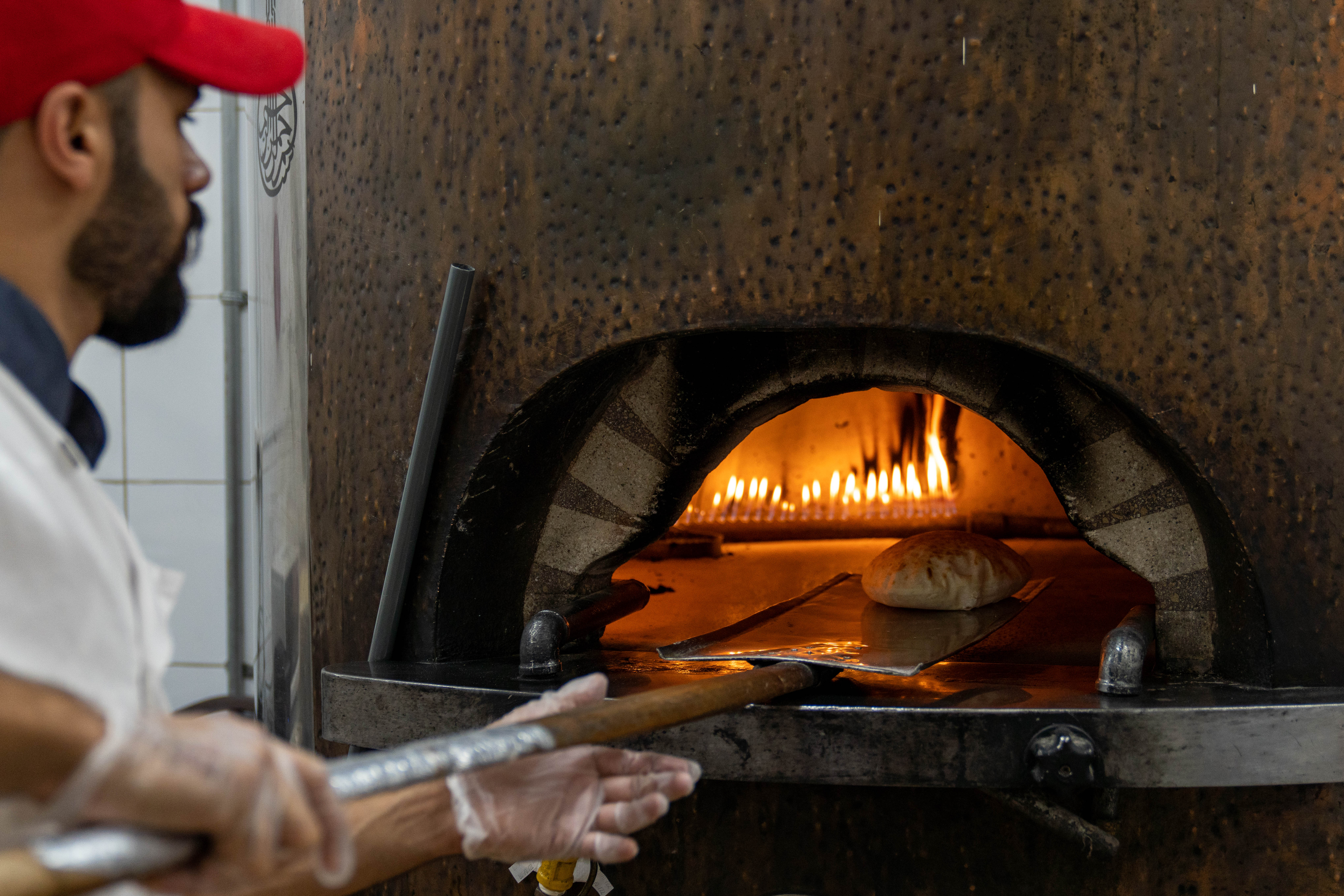 a male cook ises a long paddle to remove a freshly baked loaf of Arabic bread from the oven