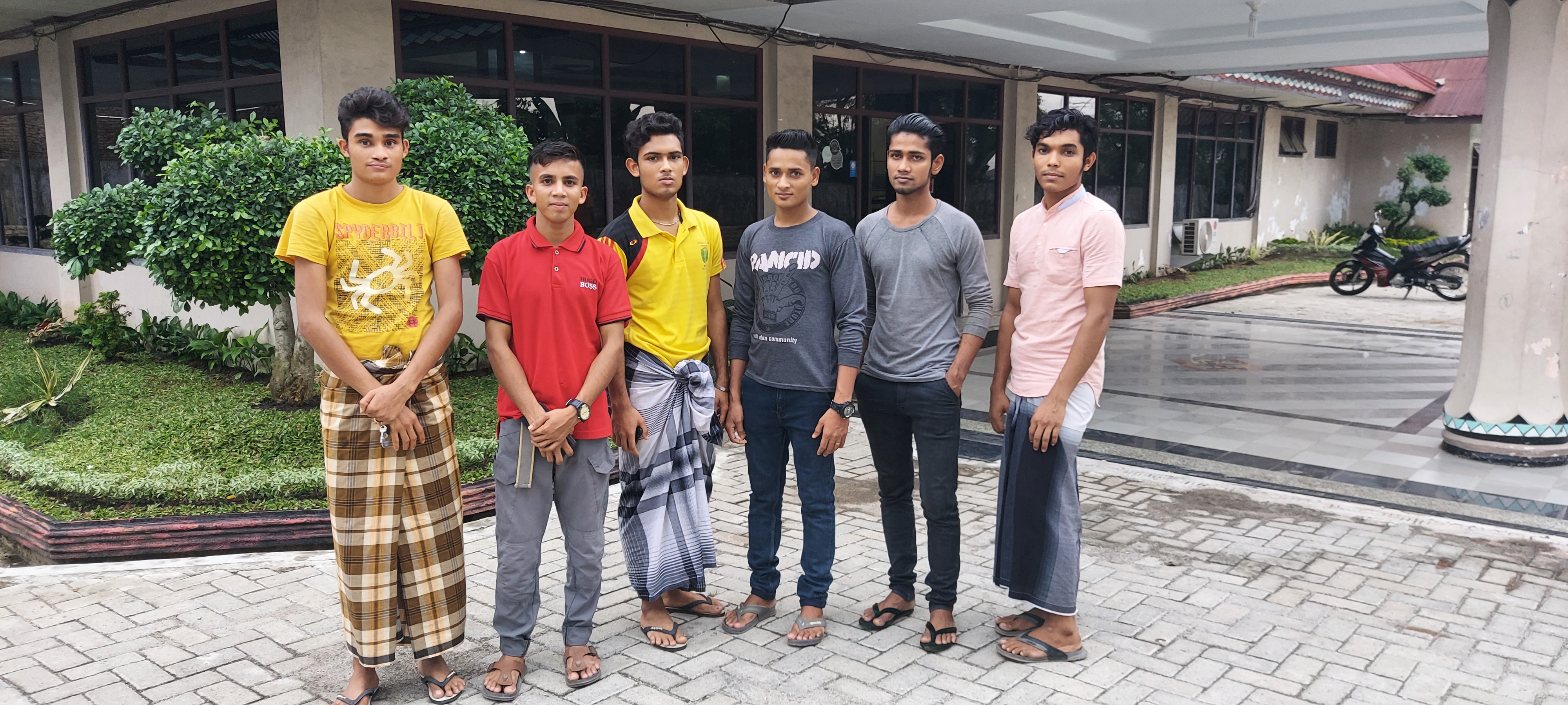 The six Rohingya men standing outside the entrance to the Hotel Pelangi. Three of them are wearing sarongs with their t-shirts and the rest trousers. They look quite pensive excpet for Gura Amin who is smiling