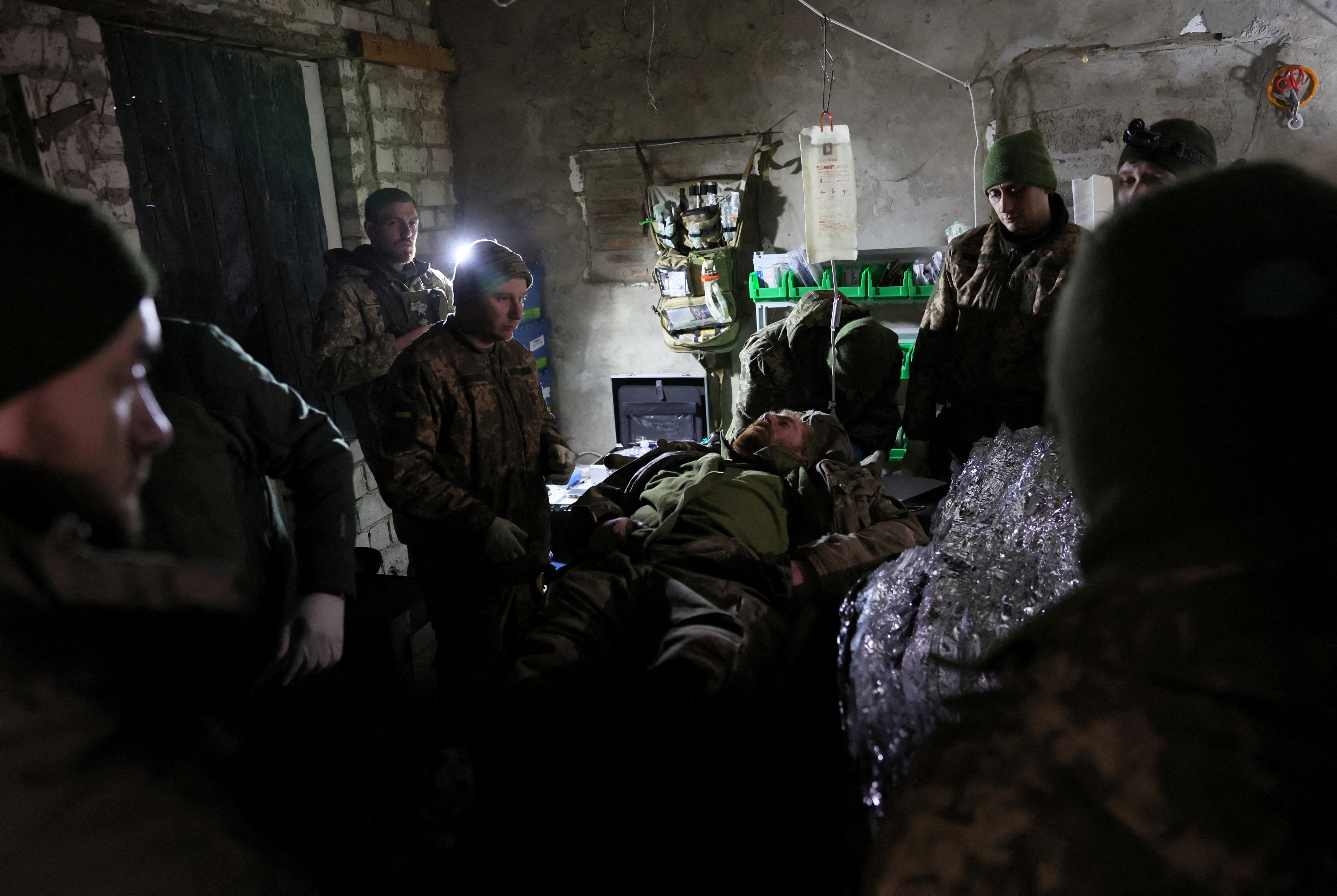 Medics at work in a field medical clinic near Bakhmut. The medics are working on an injured soldier who is lying on a bed. It is quite dark