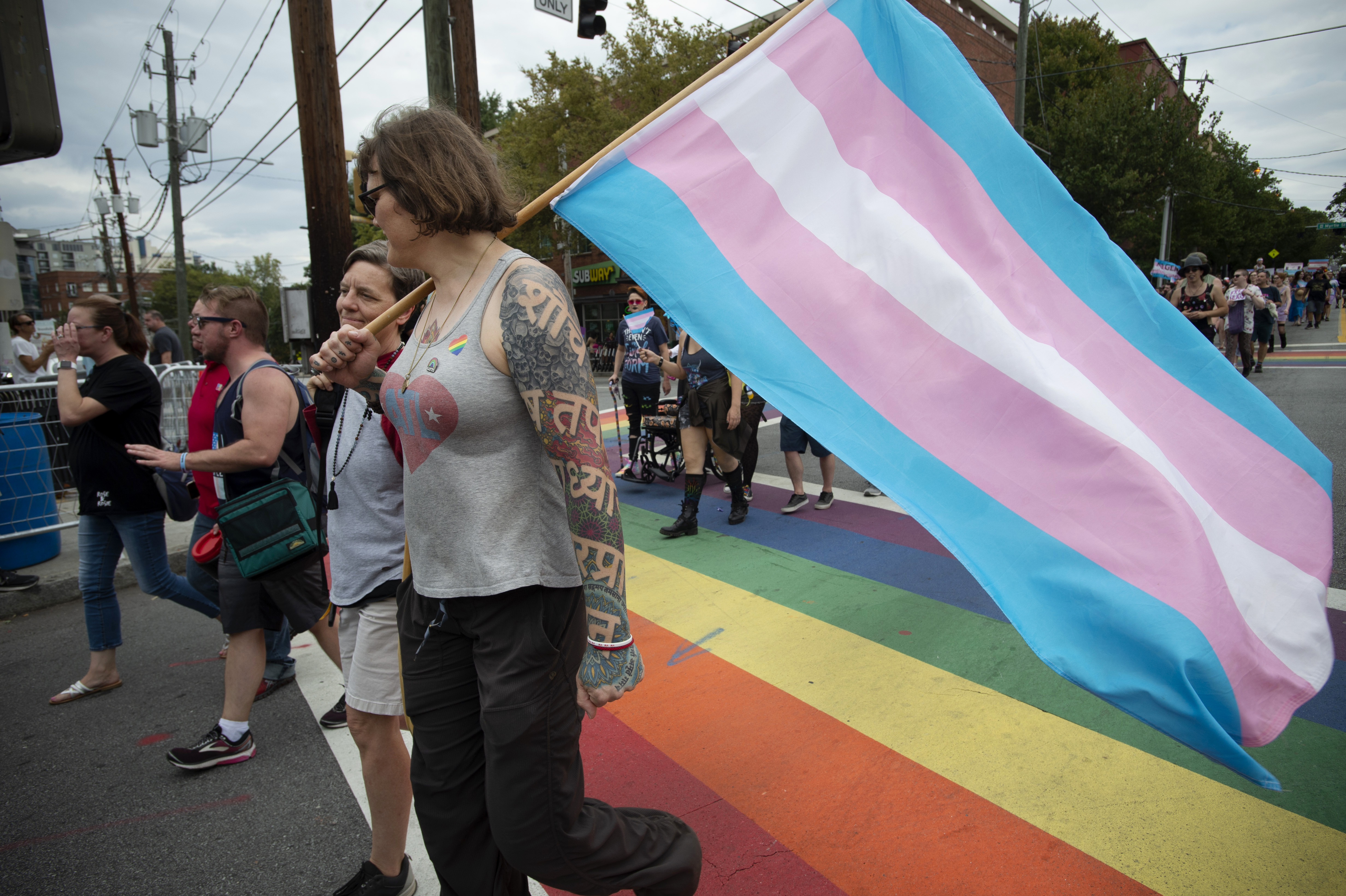 A pair of individuals walk across a rainbow-painted street in Atlanta carrying a transgender pride flag