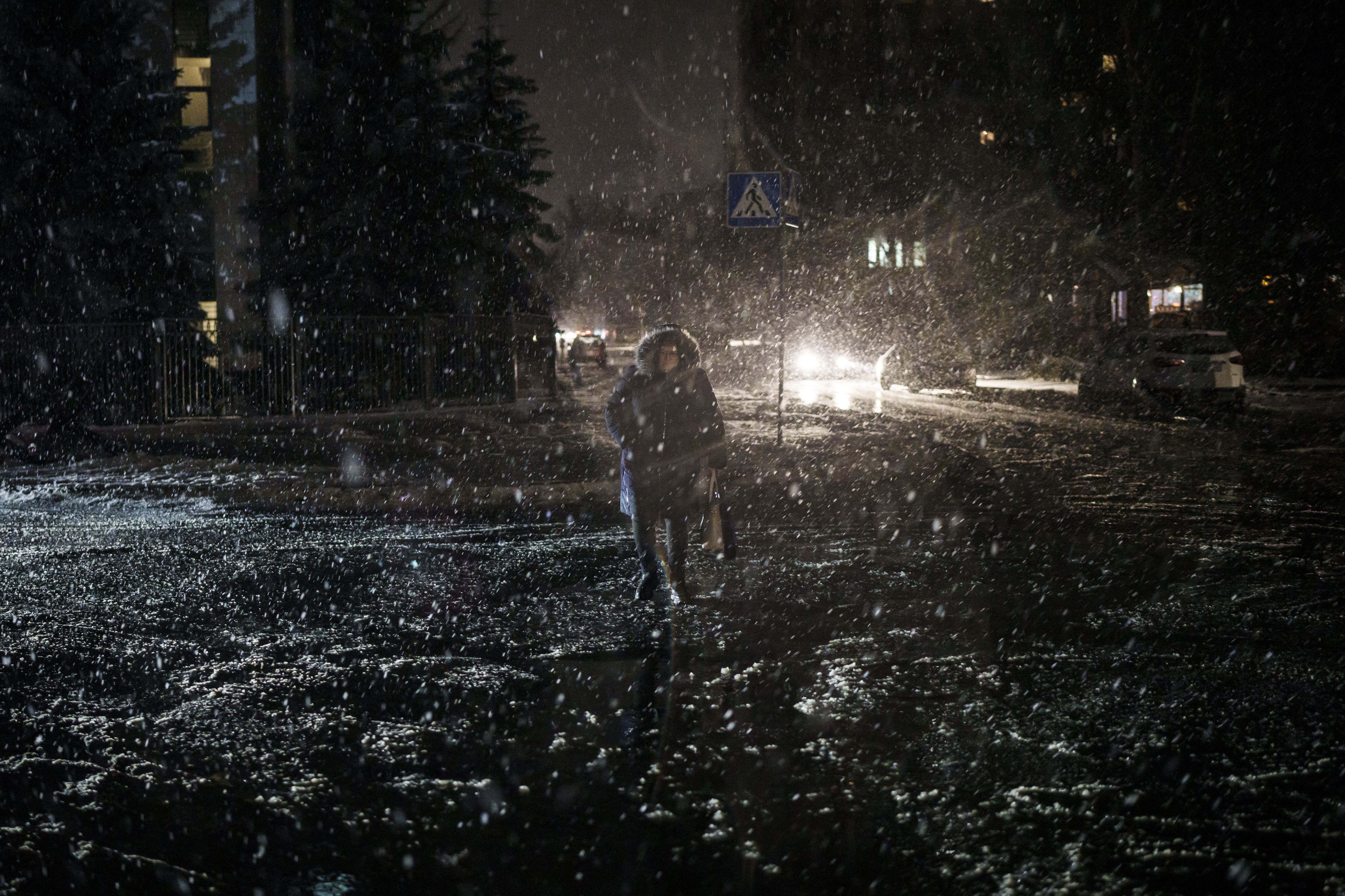 A woman crosses the street during snowfall