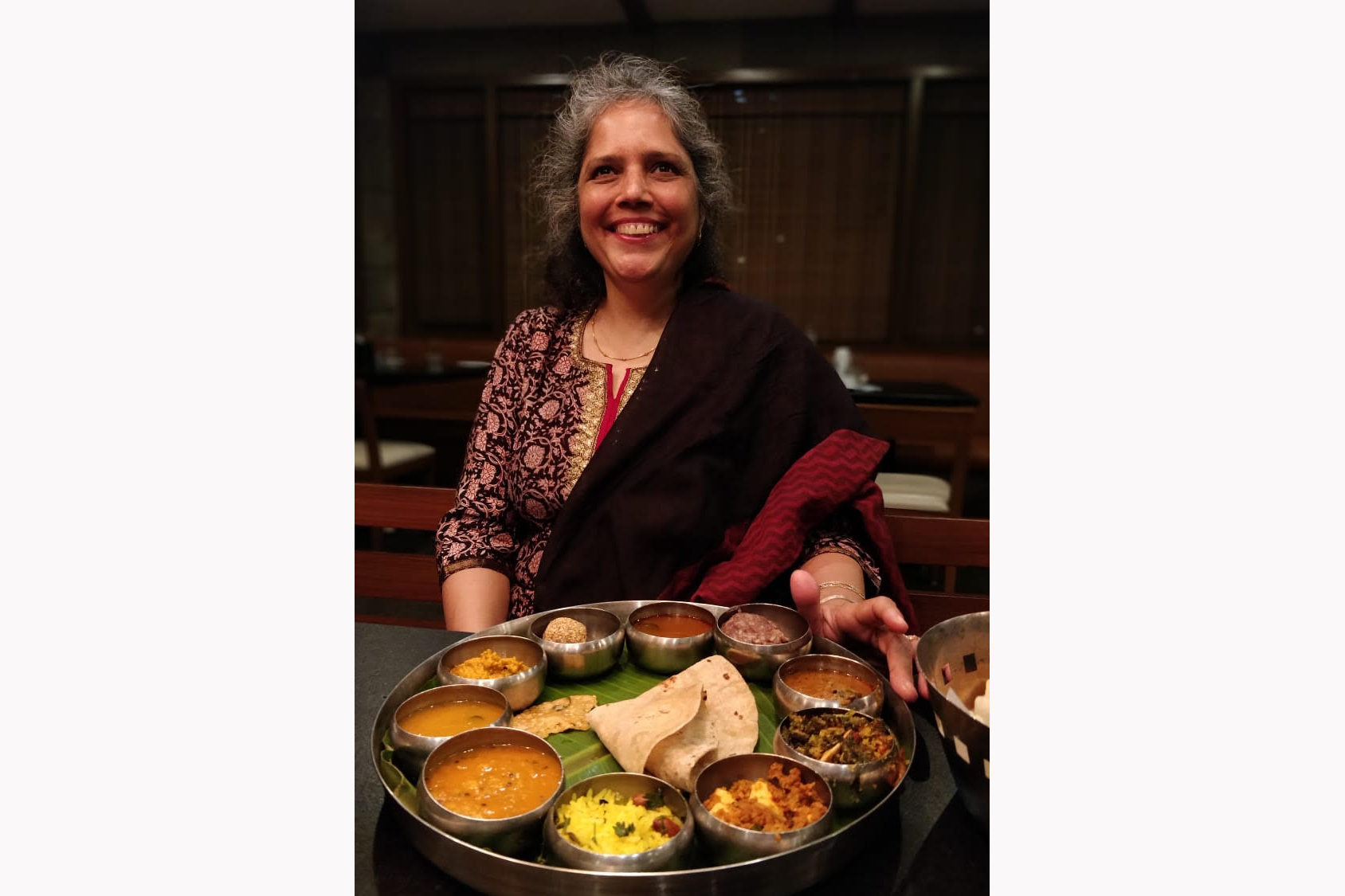 Payal smiles up at the camera with a thali in front of her, about to begin eating