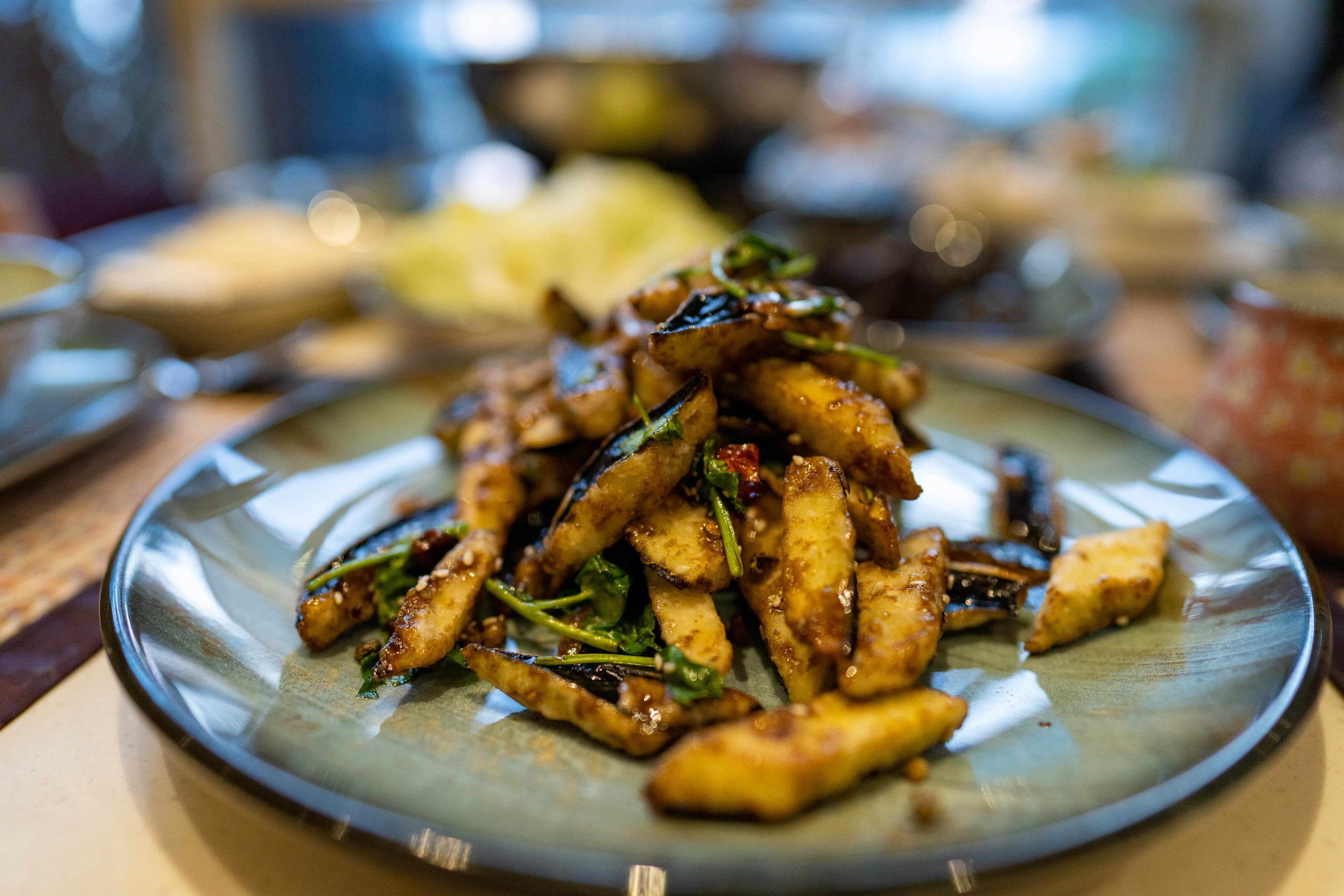 A plate of crispy eggplants seasoned with a sweet-spicy sauce and shreds of crisp chillis