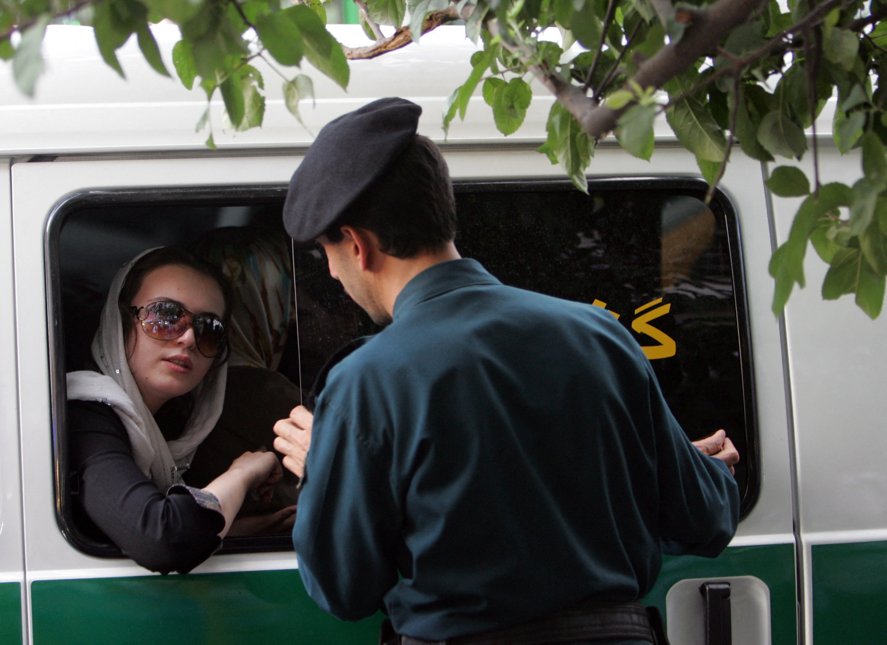 An Iranian policeman speaks with a woman in a police car after she was arrested because of her 'inappropriate' clothes