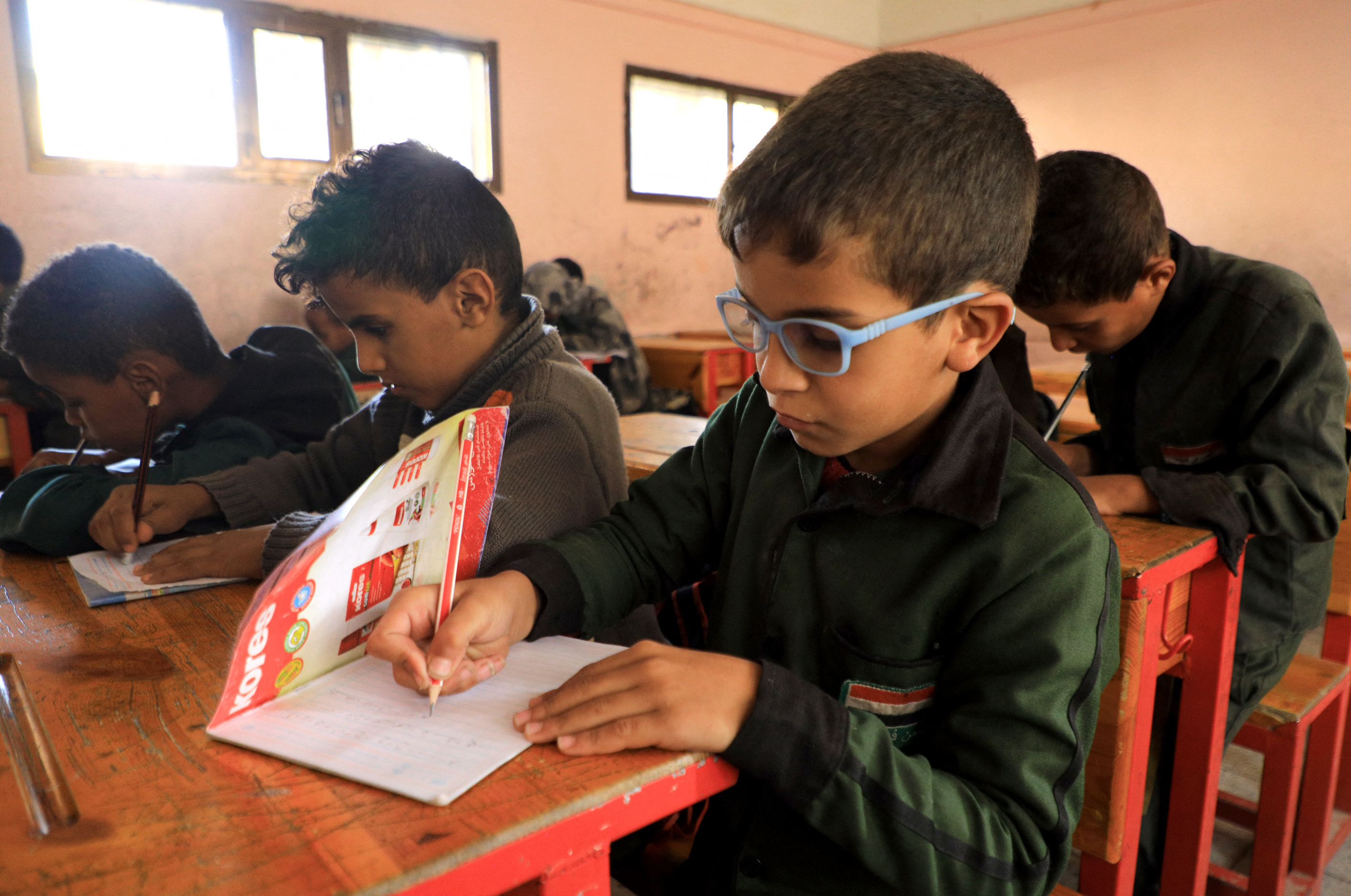 A photo of children in a classroom writing something in a notebook.