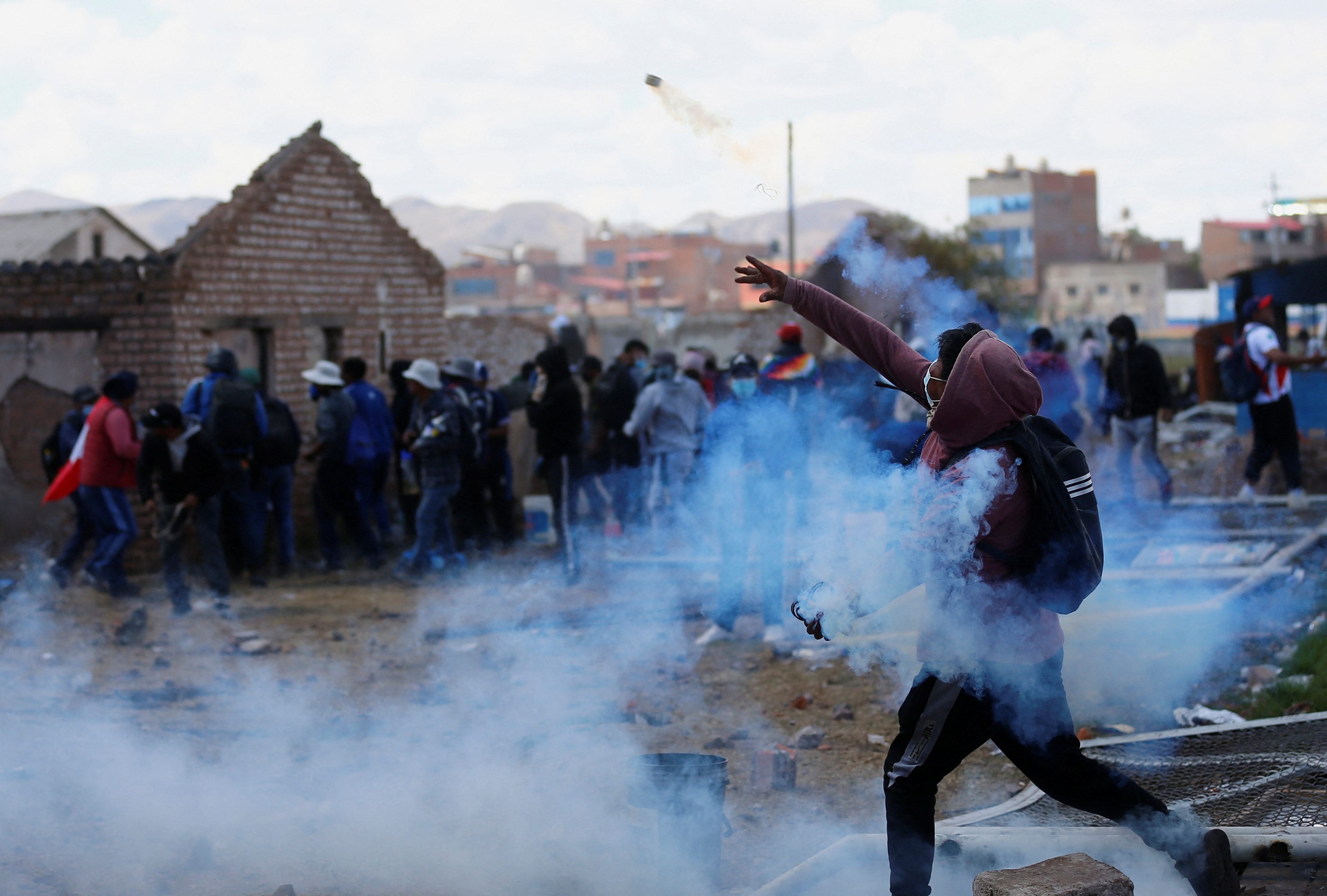 A man hurls an object towards the police during clashes in Juliaca. There are lots of other people around and smoke filling the air.