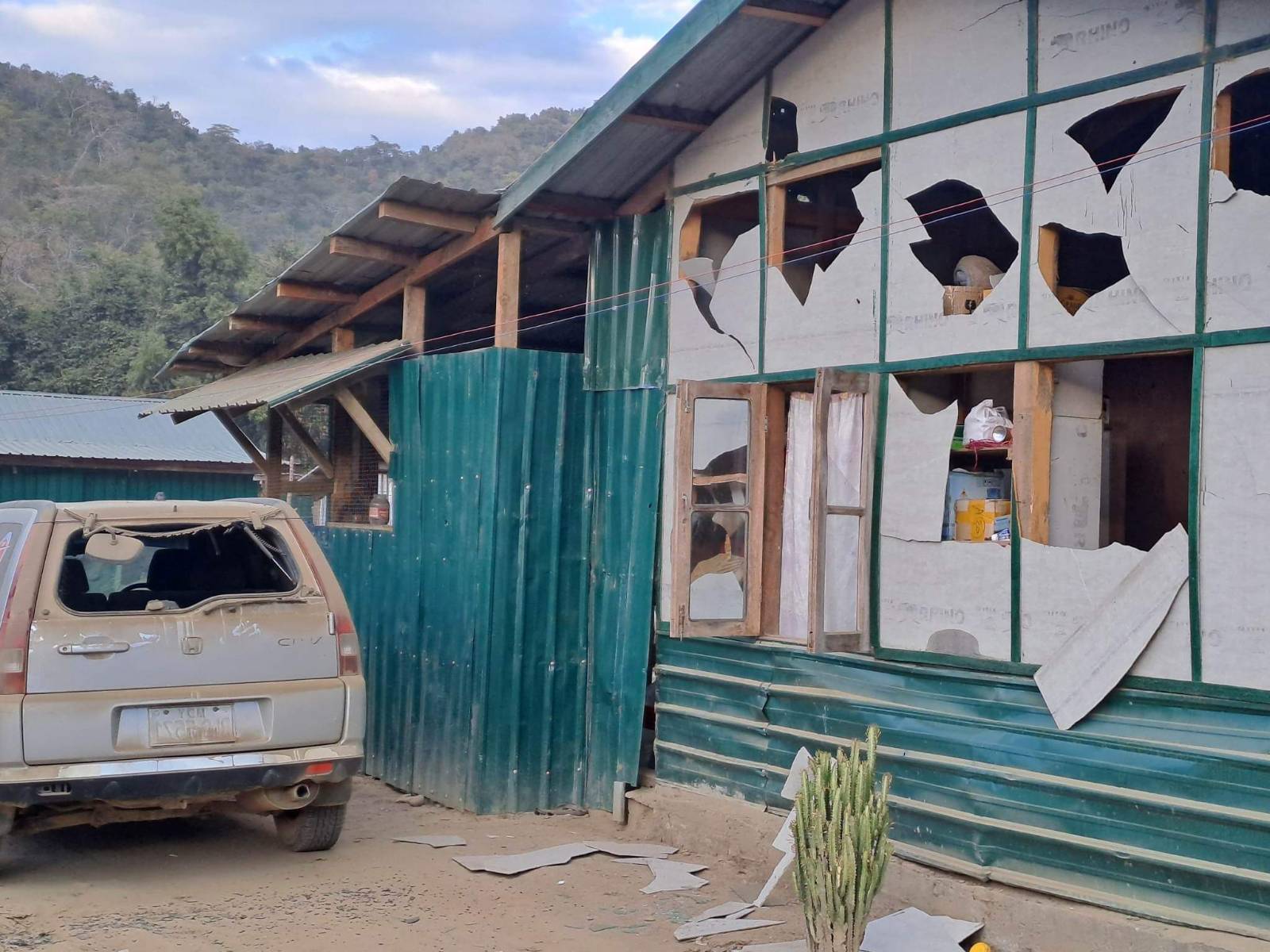 A house and car damaged by the Myanmar military attacks at Camp Victoria, The panels making up the wooden building have been broken leaving large holes. The glass in the car has been blown out