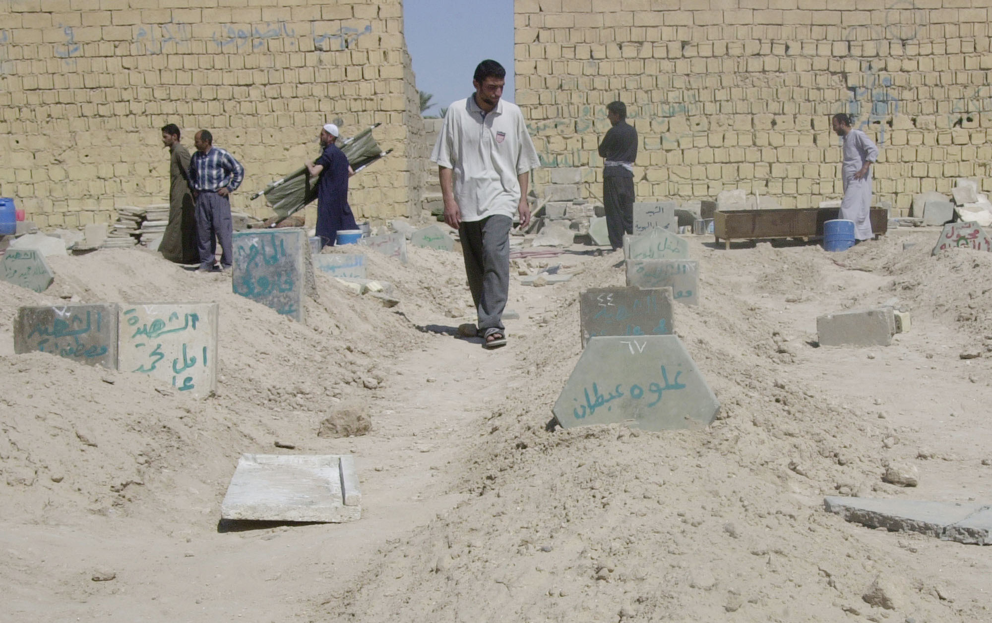 Iraqis walk through a soccer field turned into a cemetery, in Fallujah, Iraq, Sunday, April 11, 2004. More than 600 Iraqis have been killed in the fighting in Fallujah the past week, the head of the city's hospital said Sunday. (AP Photo/Abdel Kader Saadi)