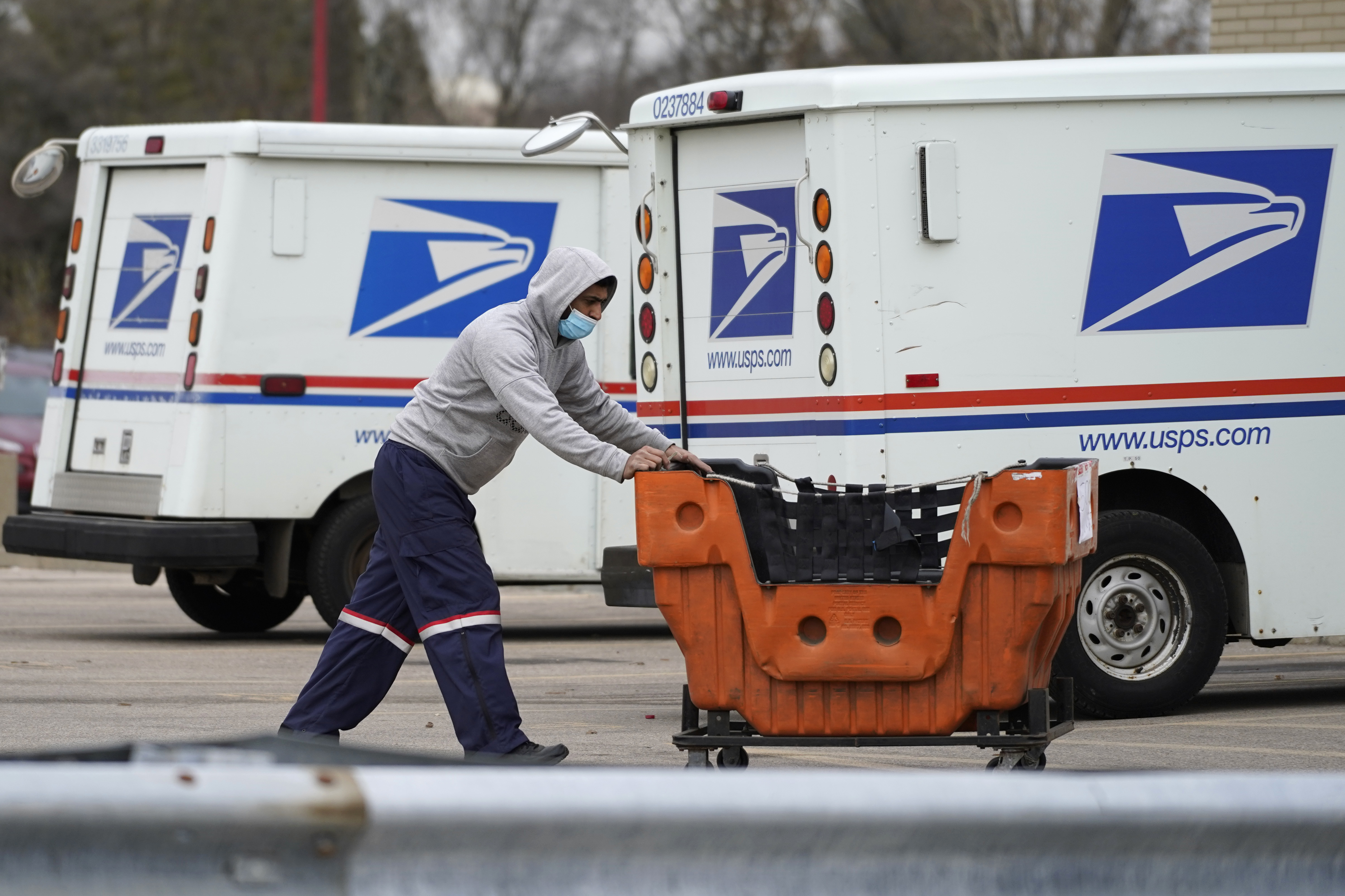 A mail carrier pushes a car through a parking lot of mail vans