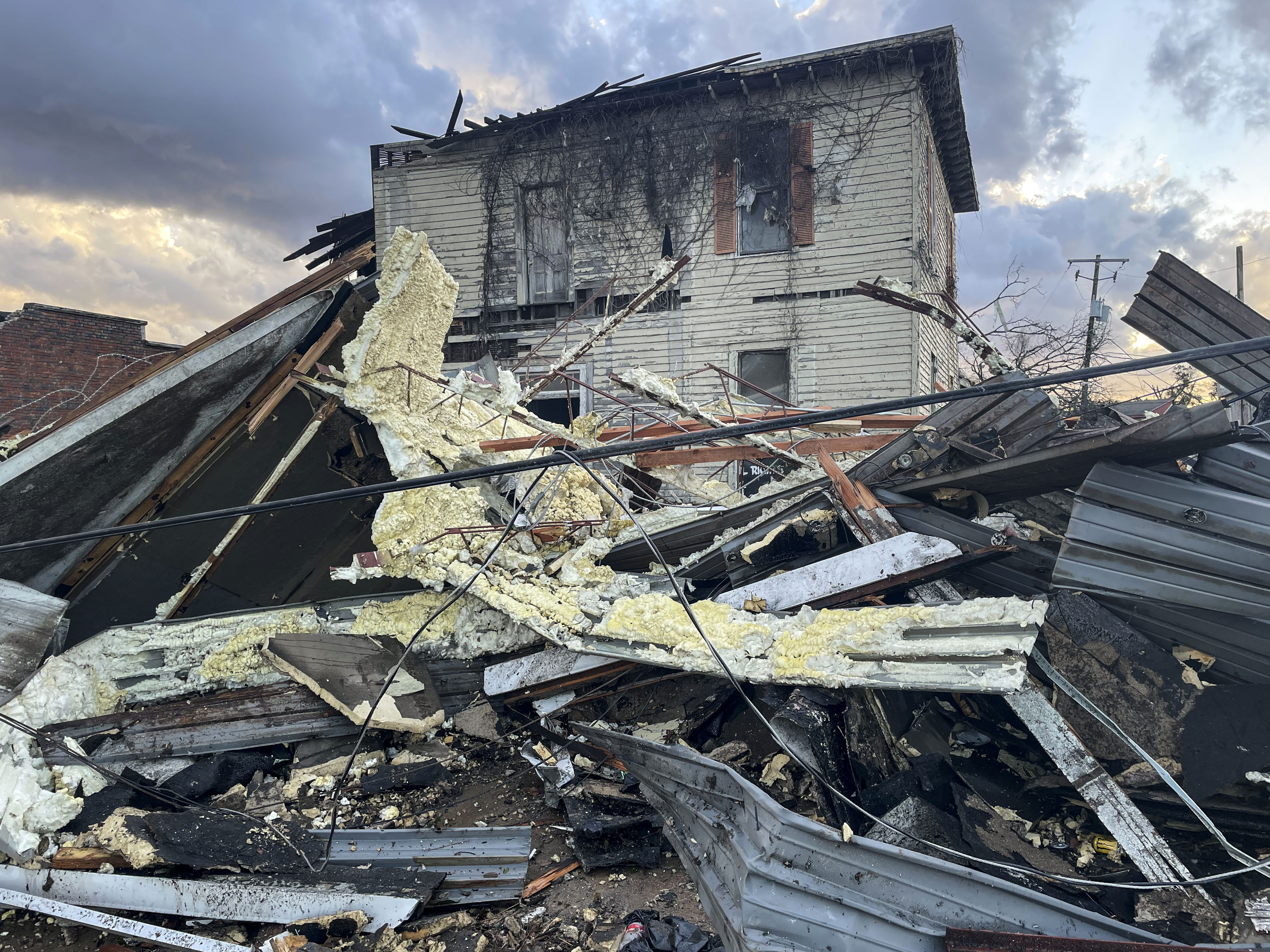 A crumpled white, wooden house in Selma, Alabama with slabs of the corrugated-iron roof and other parts of the house strewn across the forefront 
