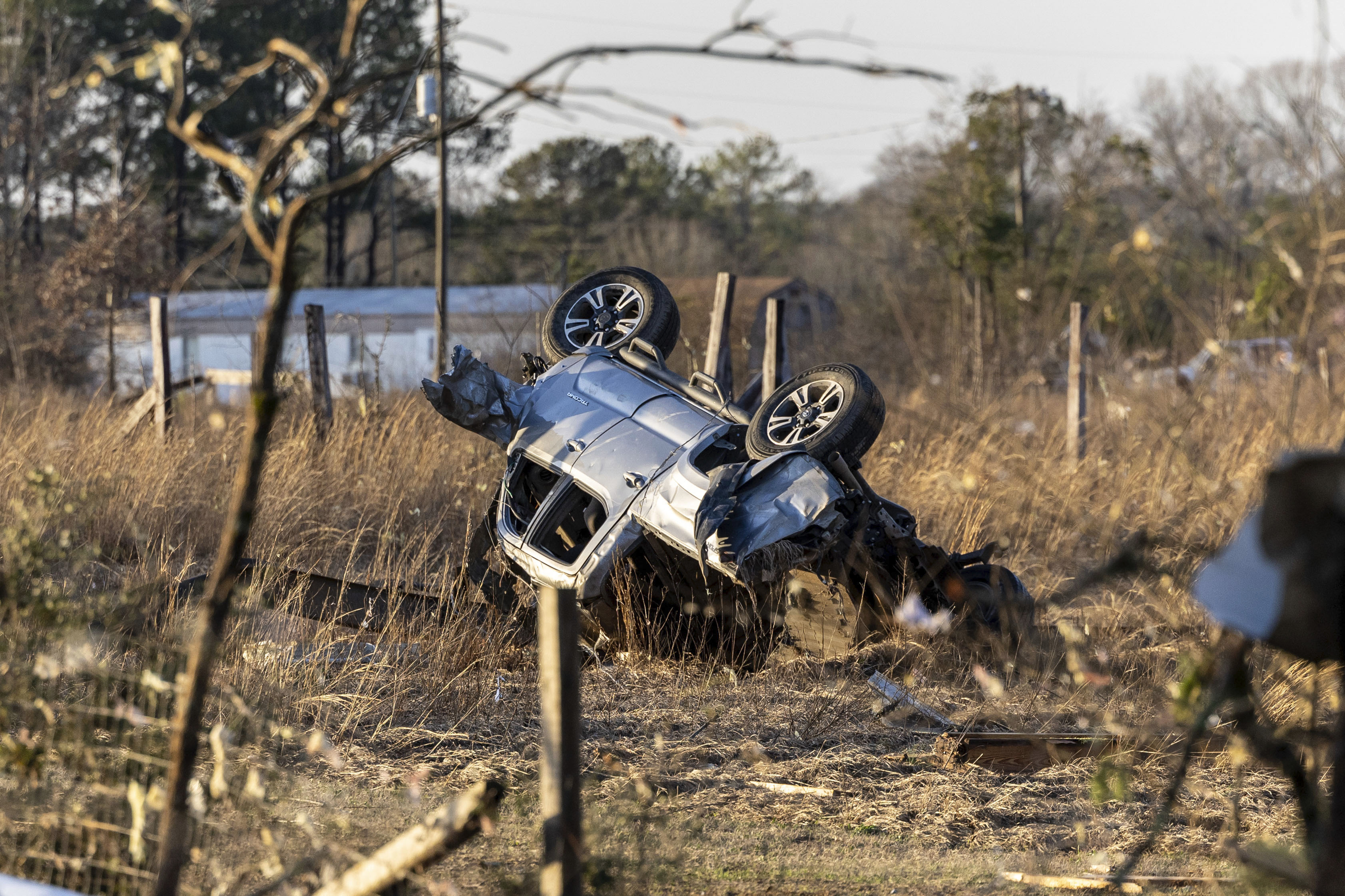 An overturned and destroyed SUV near a county road. It is lying among dry grass and twigs
