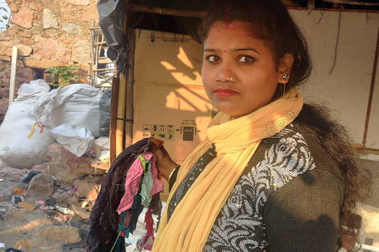 A photo of a woman standing outside holding some wet fabric with a couple of white garbage bags in the background.