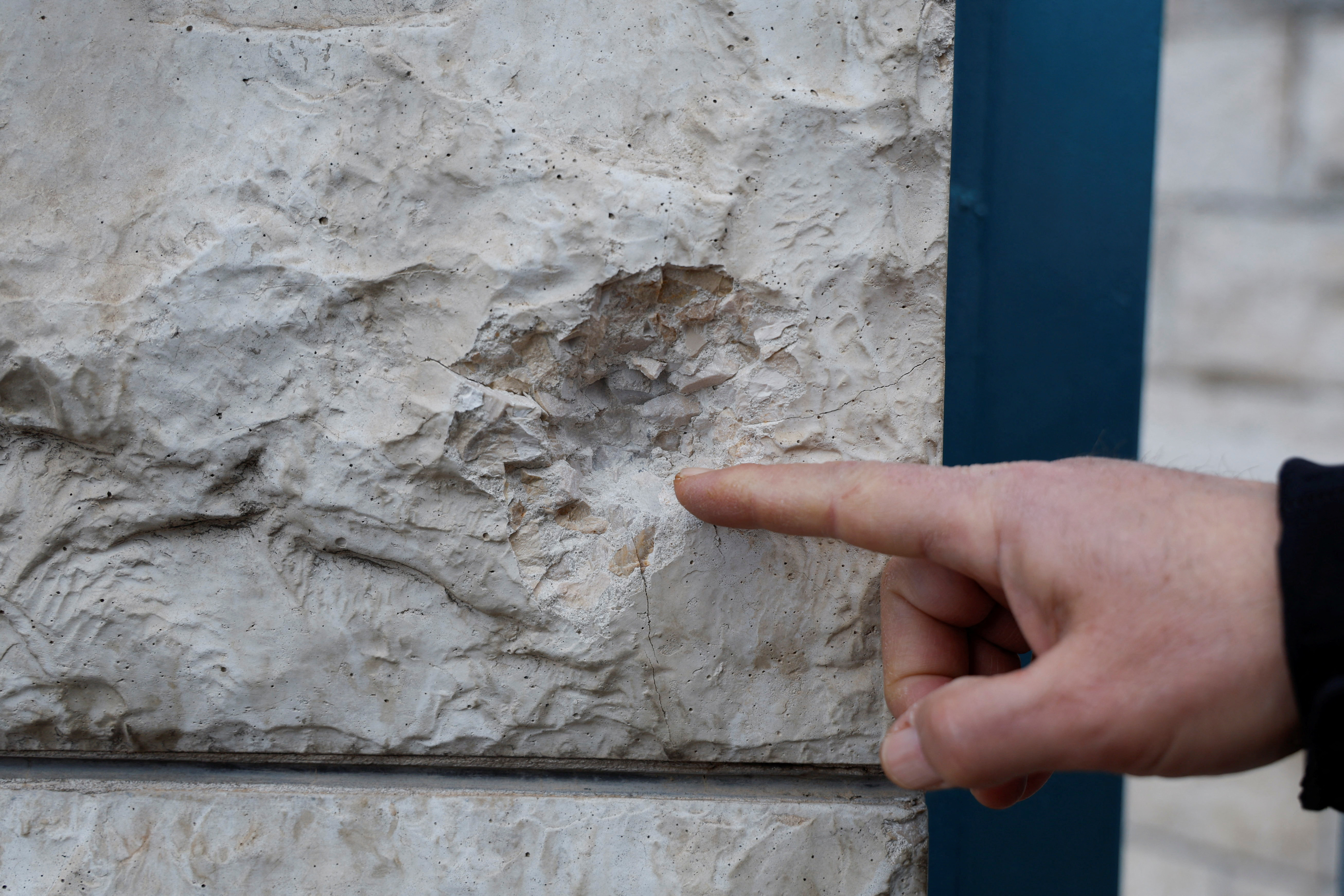 A person points to a bullet mark in the wall
