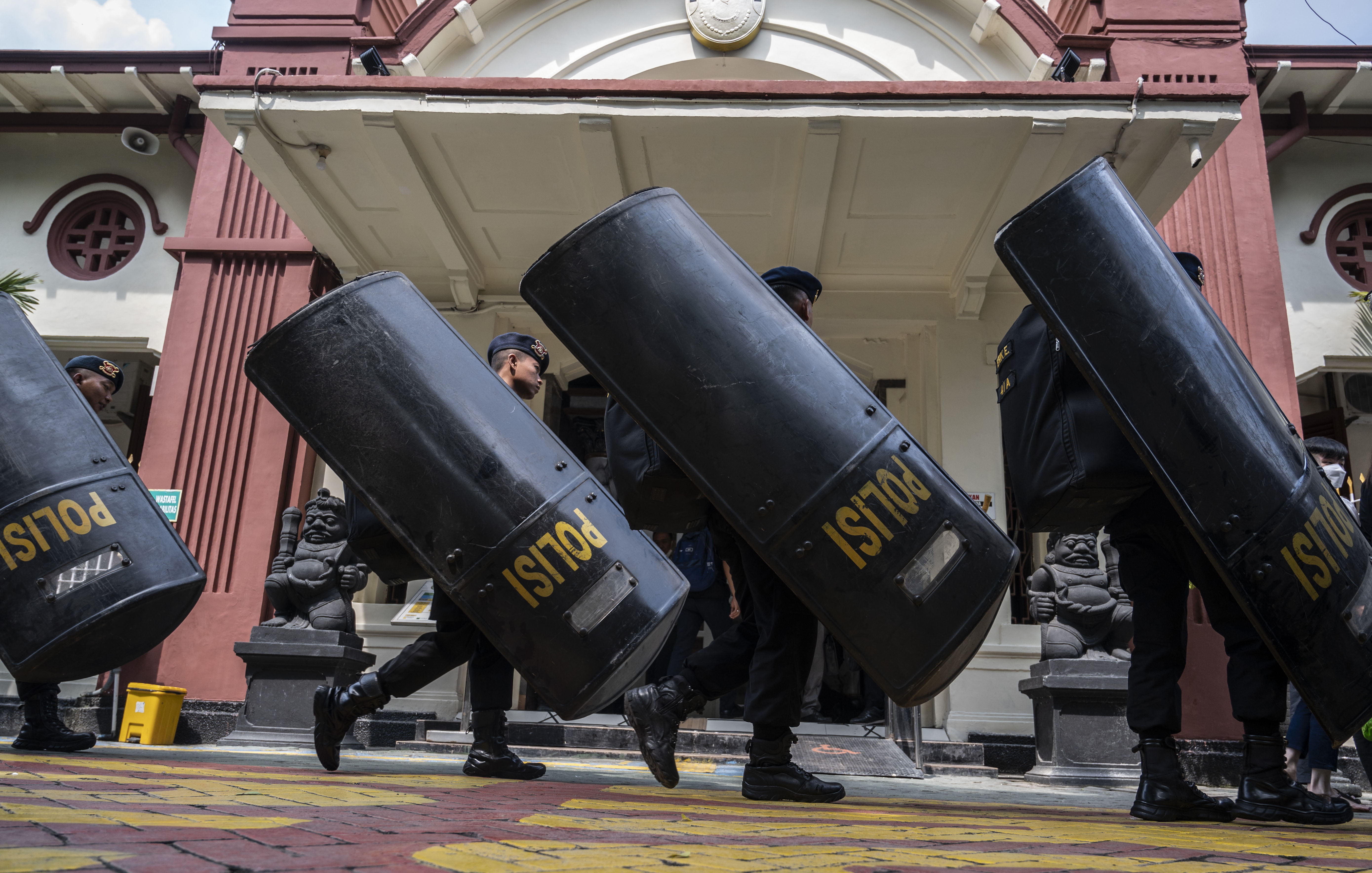 Police moving into position with riot shields outside the court in Surabaya. The shields are black and have the word POLISI written on them in yellow.