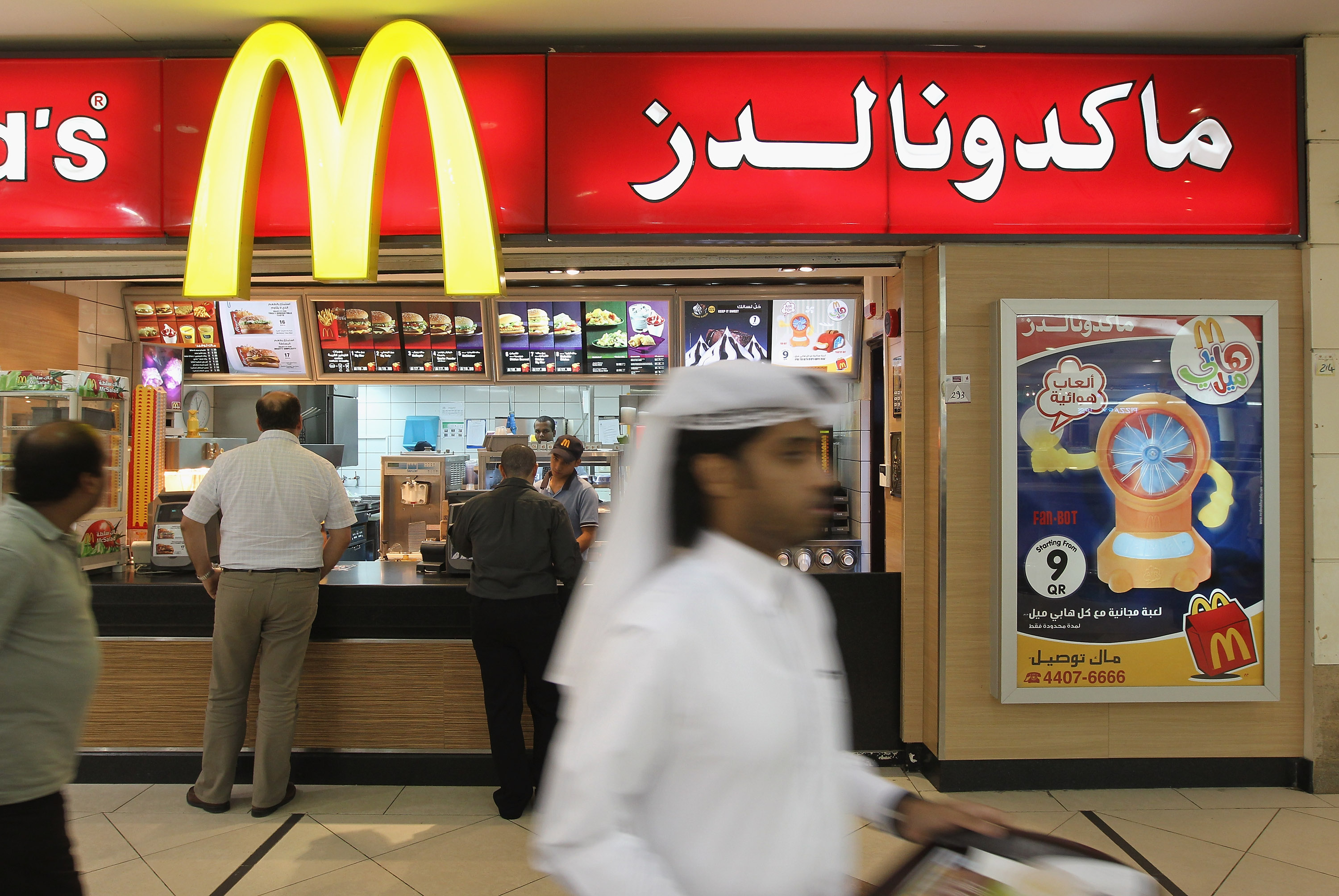 A man wearing traditional local clothes carries a tray of food from a McDonald's fast food restaurant.