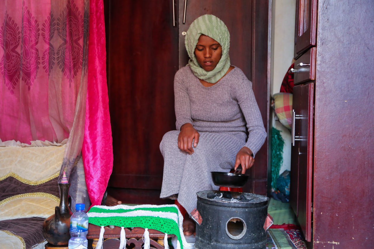 A photo of a woman making coffee using a pot on a stove.