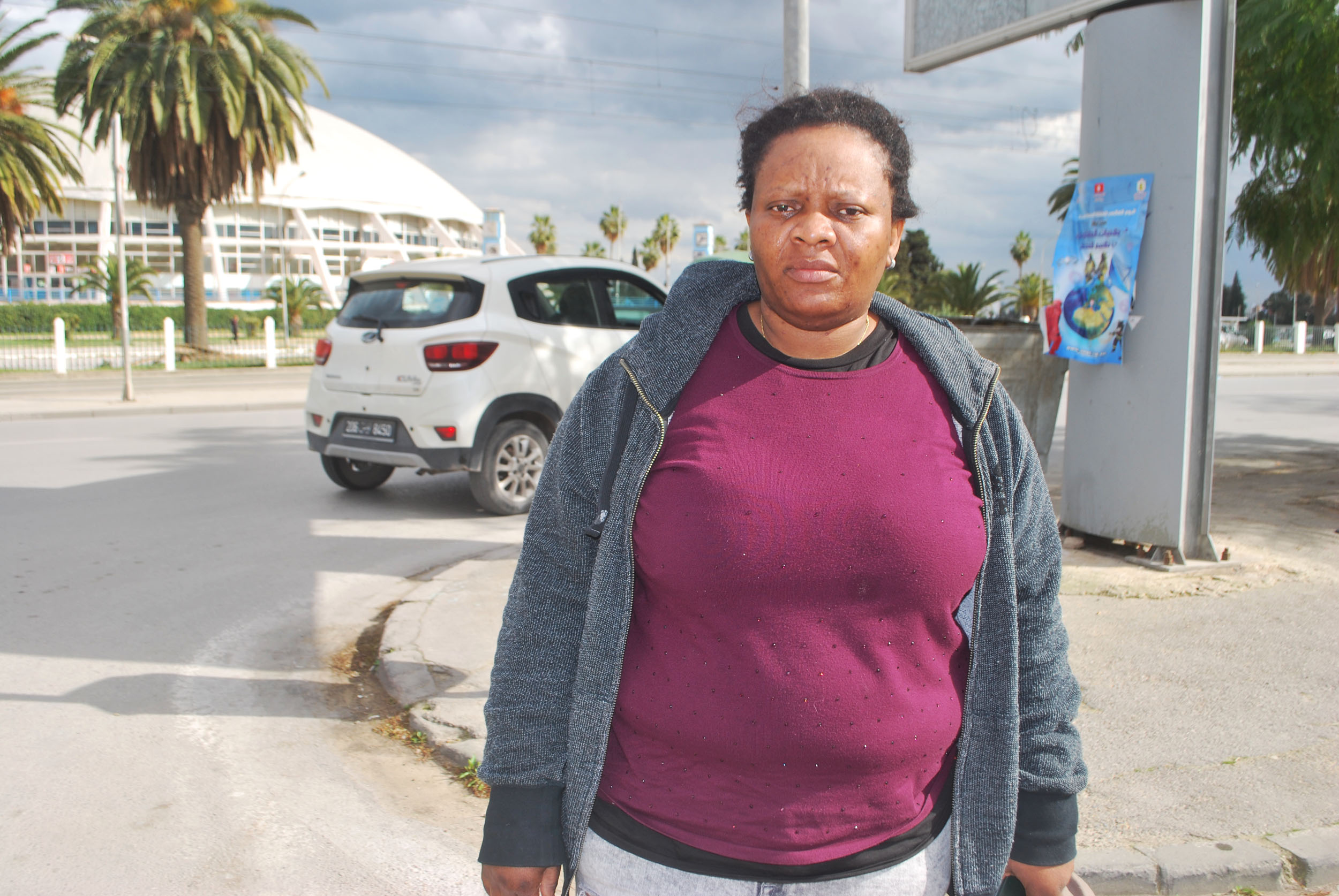 Congolese migrant Nikky Yanga stands on the side of a road as a car passes behind her.