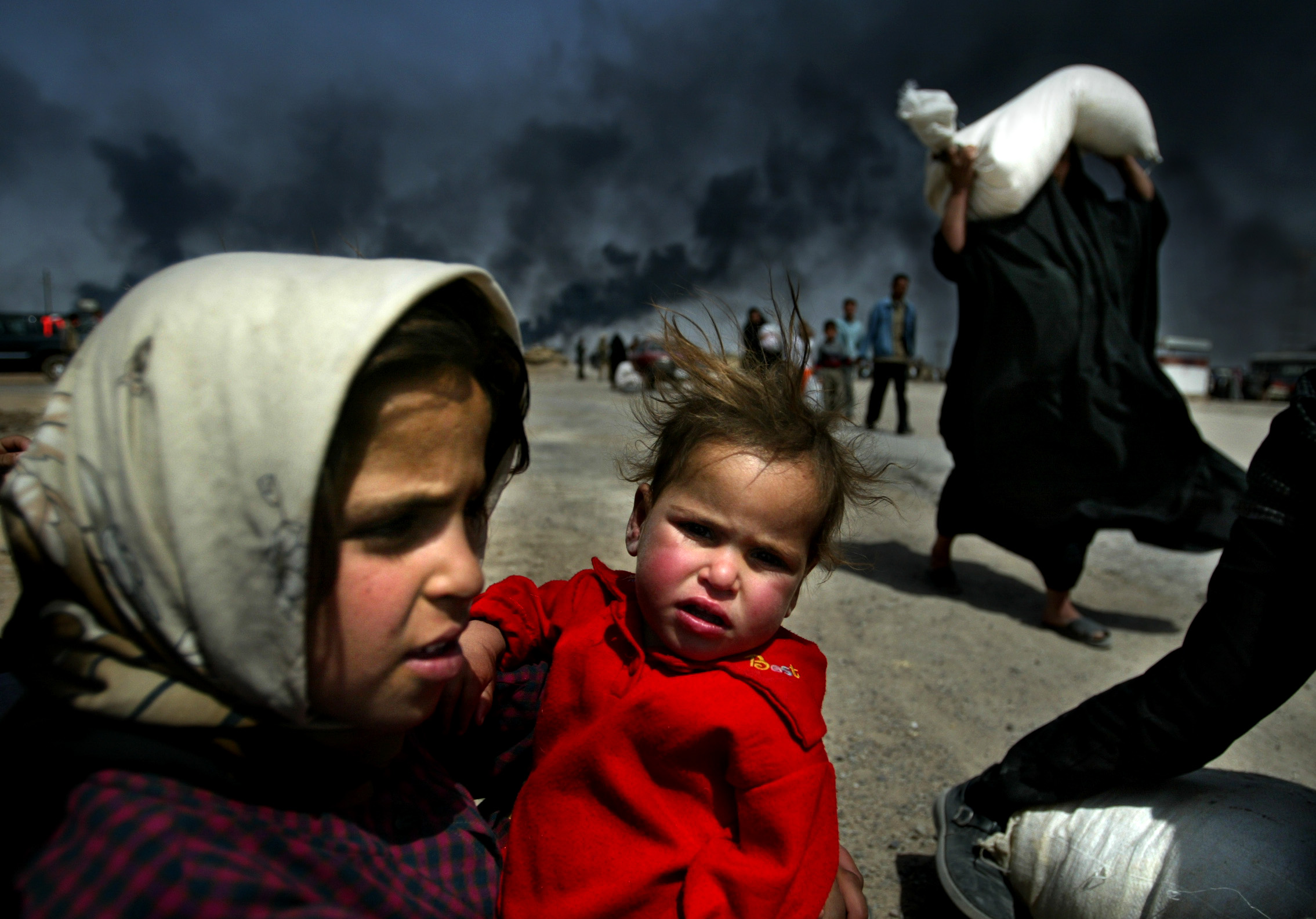 An Iraqi girl holds her sister as she waits for her mother to bring over food she is buying, in Basra on March 29, 2003