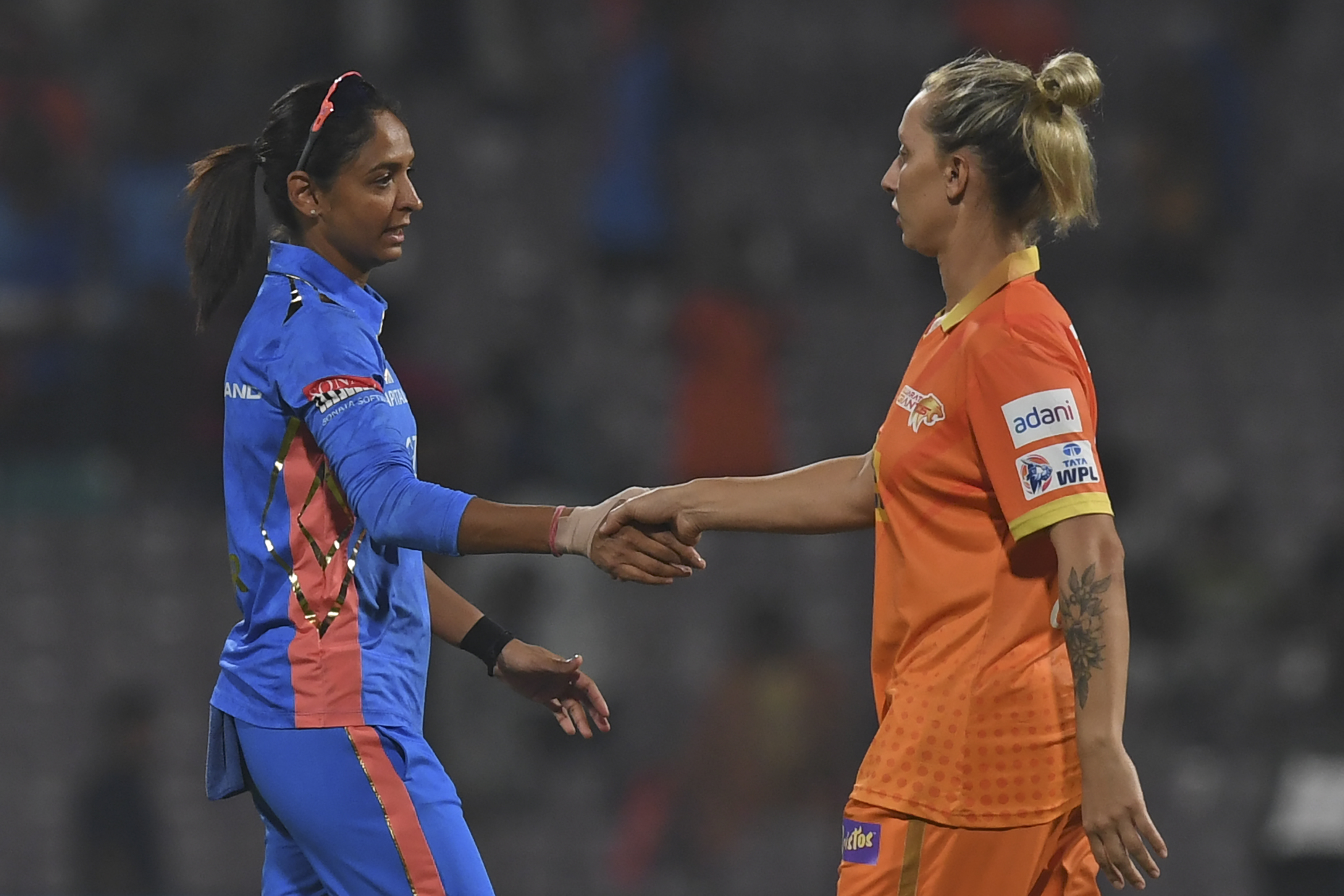 Mumbai Indians' captain Harmanpreet Kaur (L) shakes hands with Gujarat Giants' Ashleigh Gardner at the end of the 2023 Women's Premier League (WPL) Twenty20 cricket match between Gujarat Giants and Mumbai Indians at the DY Patil Stadium in Navi Mumbai on March 4, 2023
