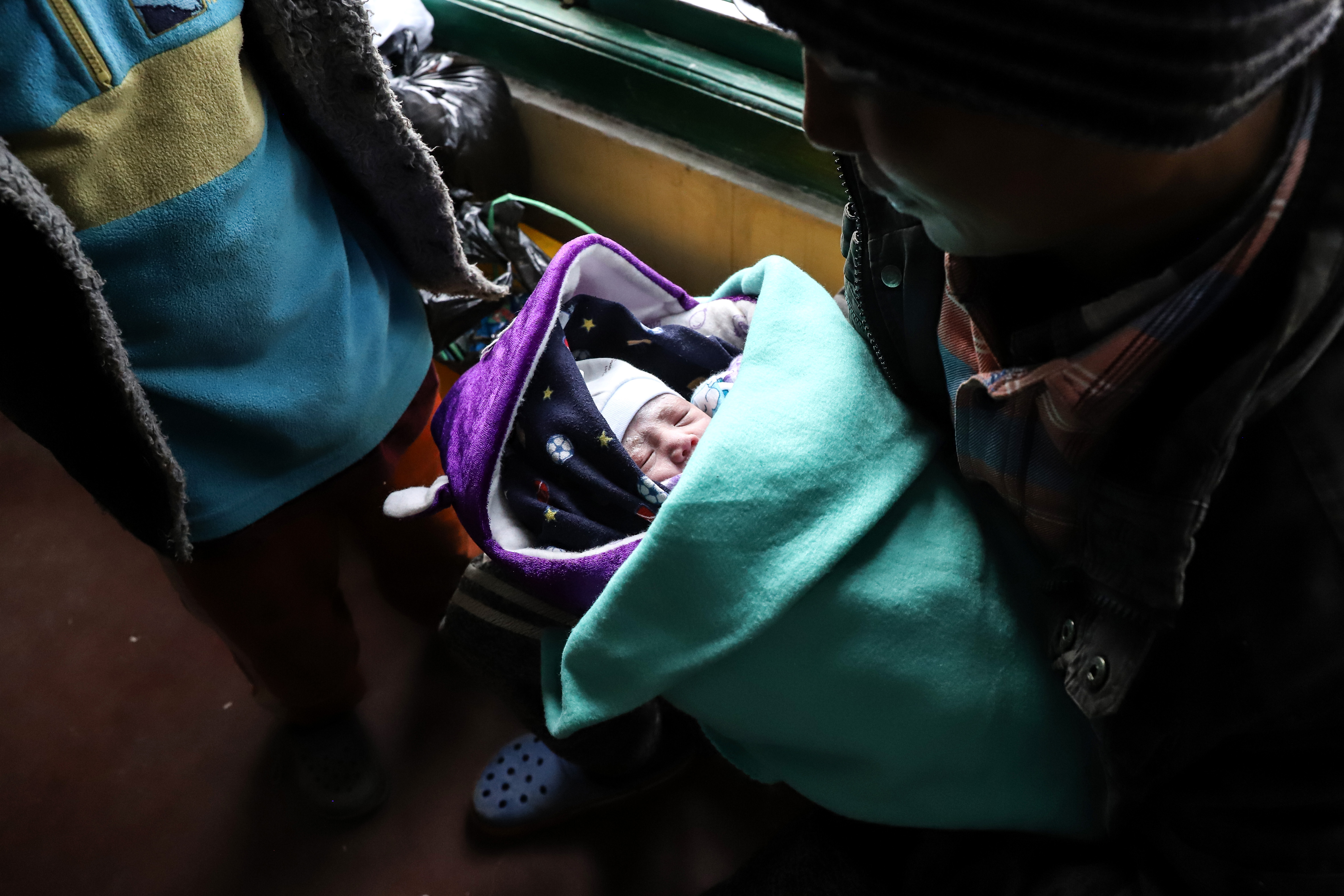 Aung Pyae looking at his baby. The child is wrapped in blankets of green and blue and there's a purple hood.