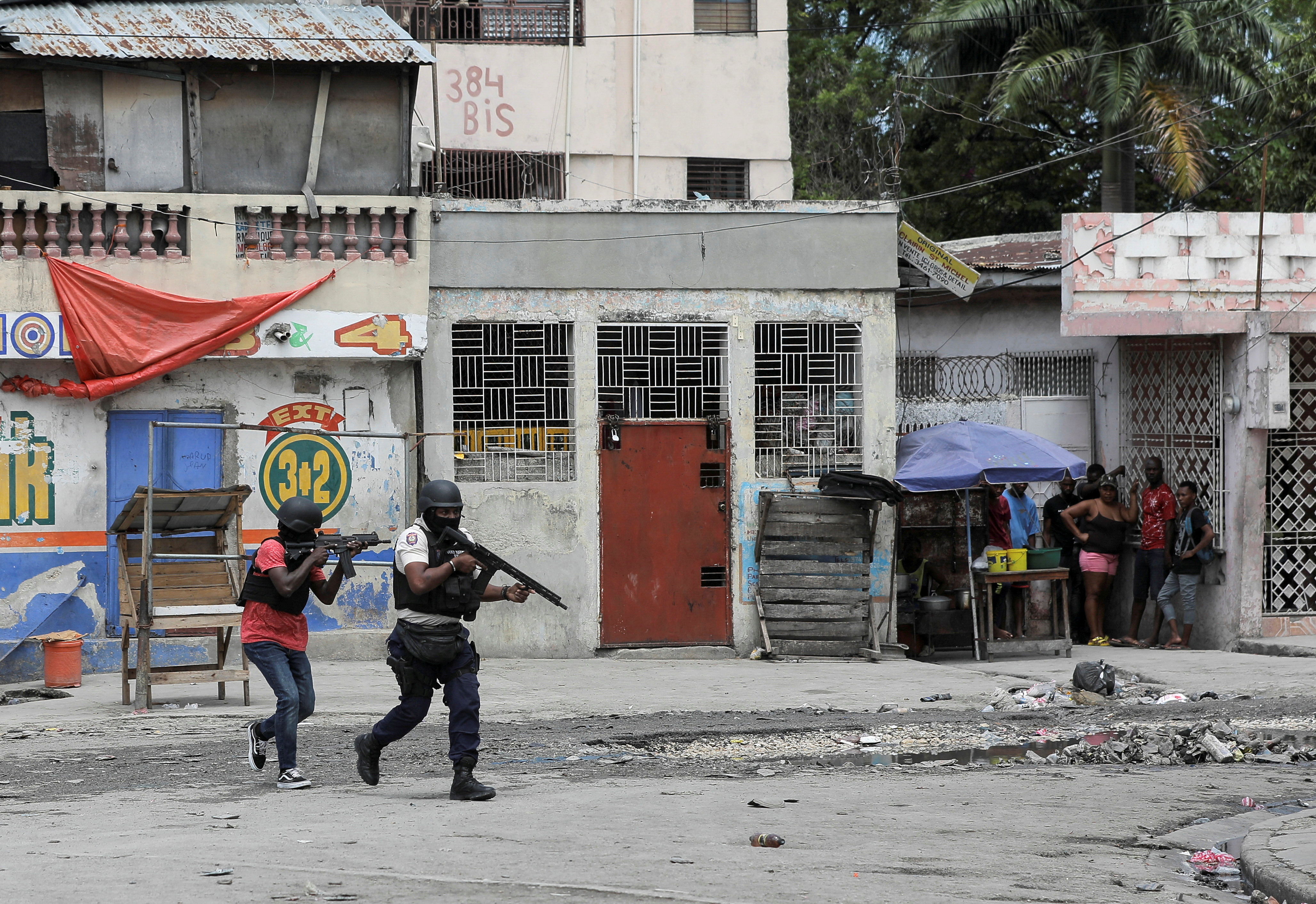 People huddle in a corner as police patrol the streets of Port-au-Prince