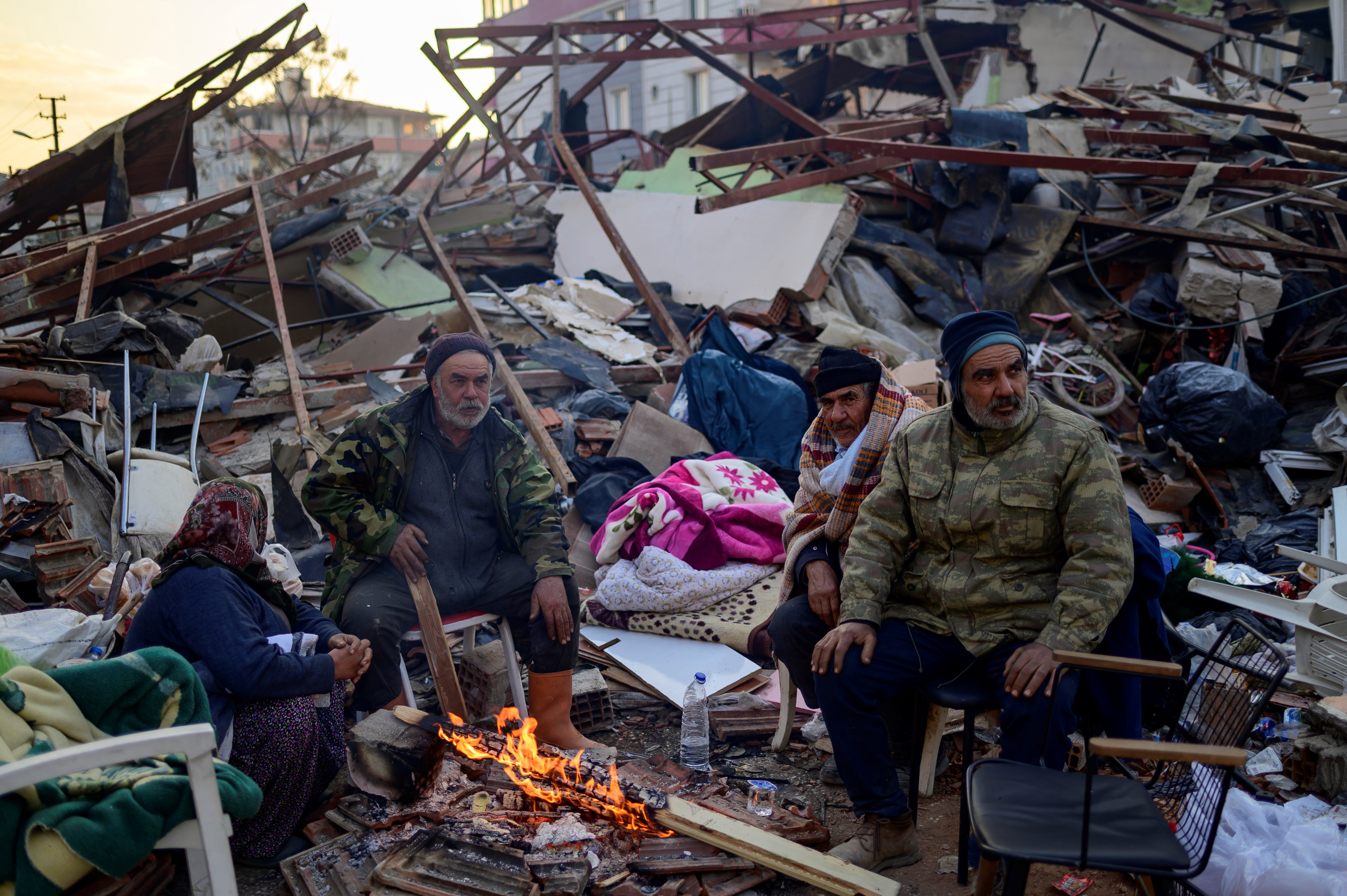 People stand by a fire among the rubble of collapsed building in Hatay, on February 10, 2023, four days after a 7.8 magnitude earthquake