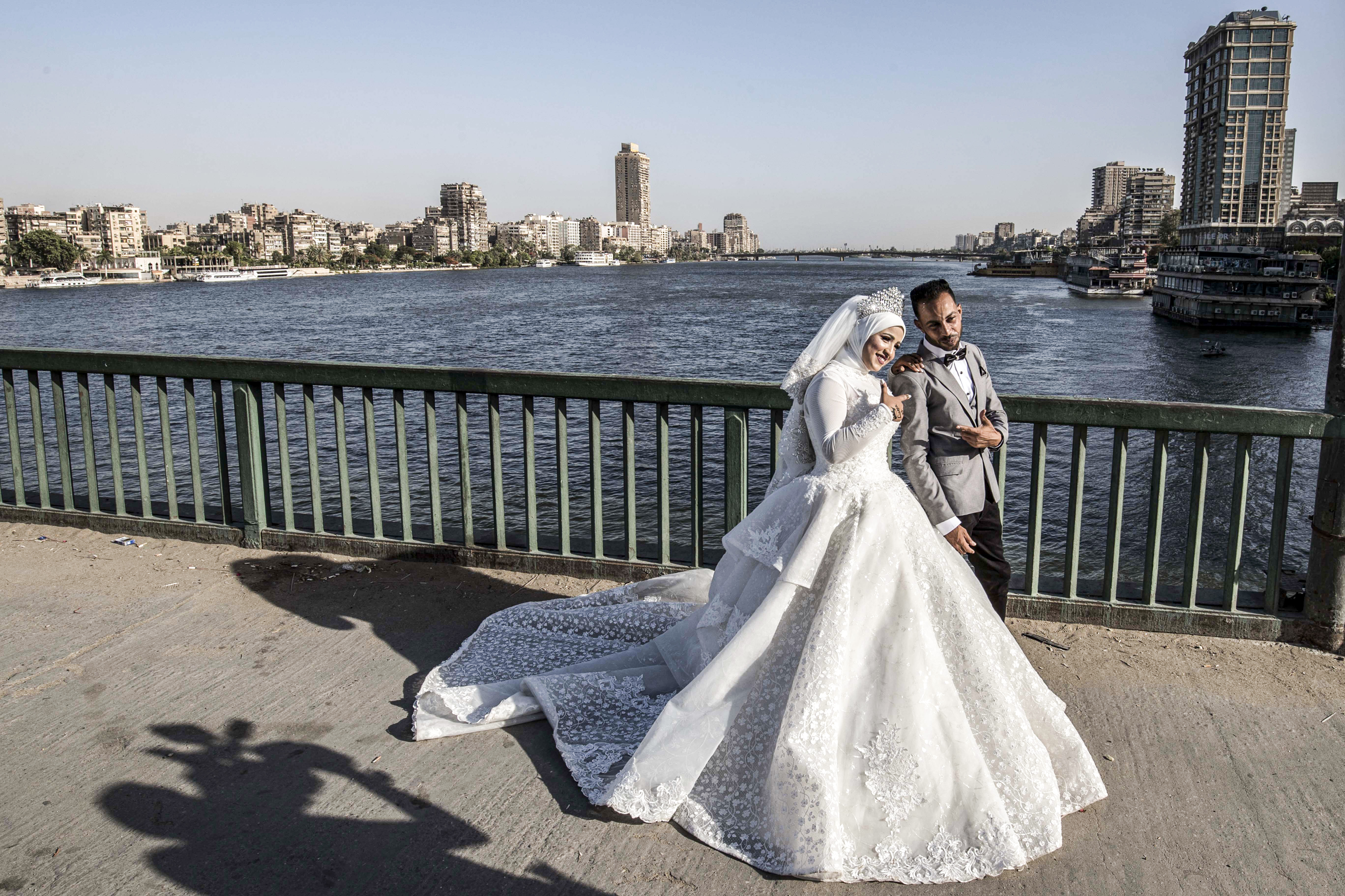 a couple poses before a video cameraman for their wedding video along a bridge by the Nile