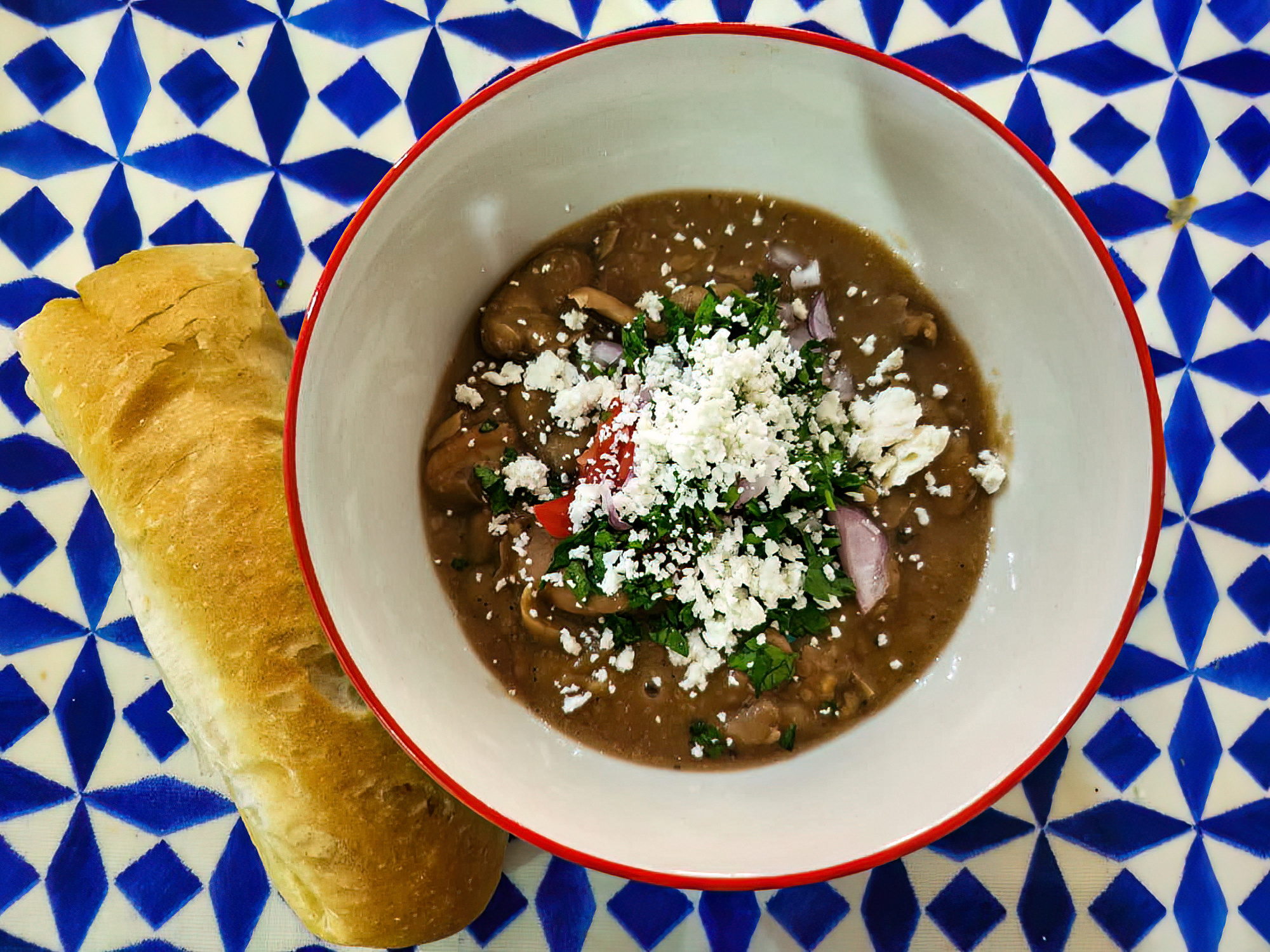 A bowl of all-dressed fuul on a blue-and-white surface with a stick of bread