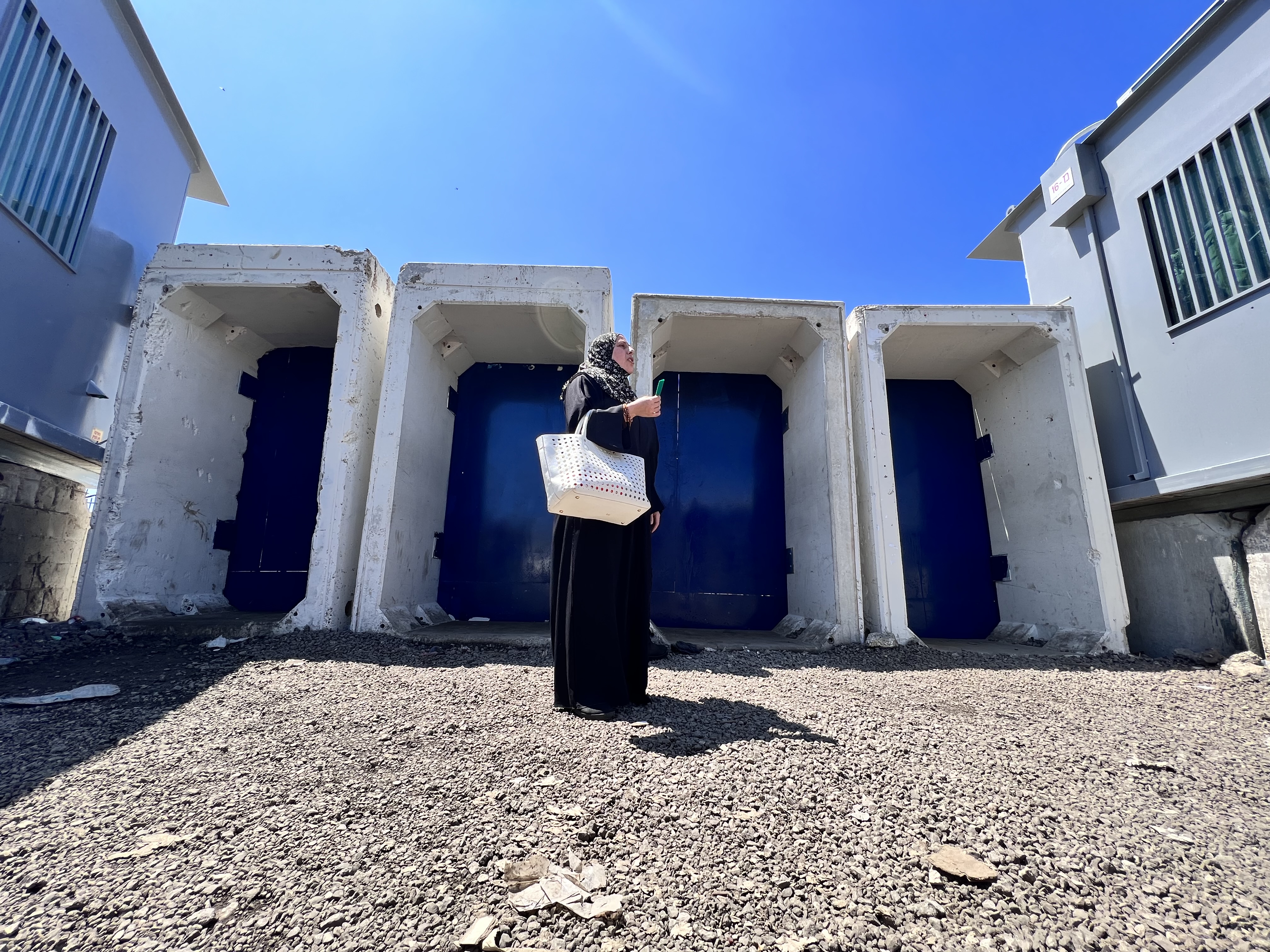 A woman stands at Qalandiya checkpoint holding her identity card