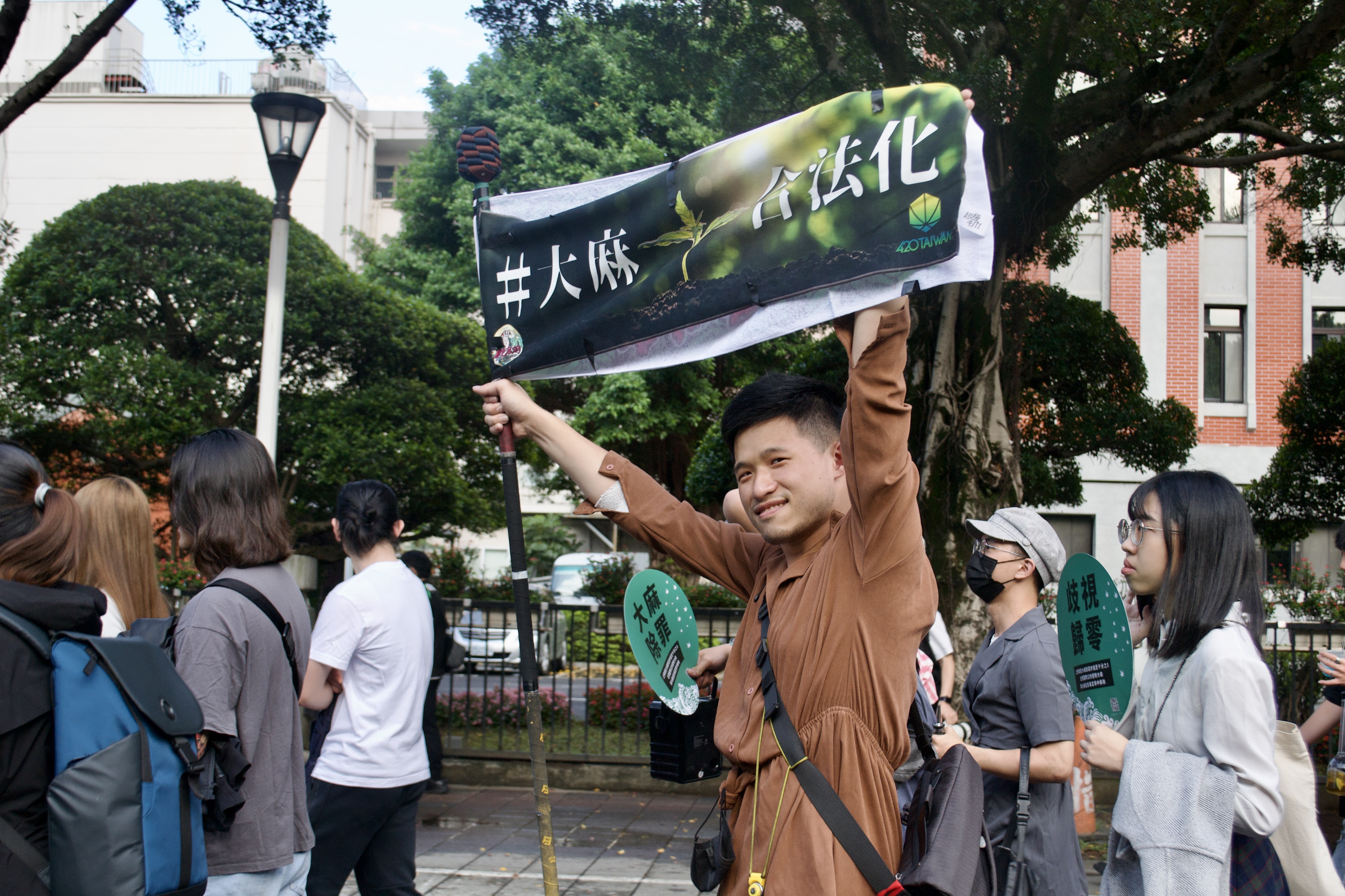 Protestors marching in Taiwan. One young man, perhaps the age of a college student, in a brown shirt is holding up a banner with both his arms.