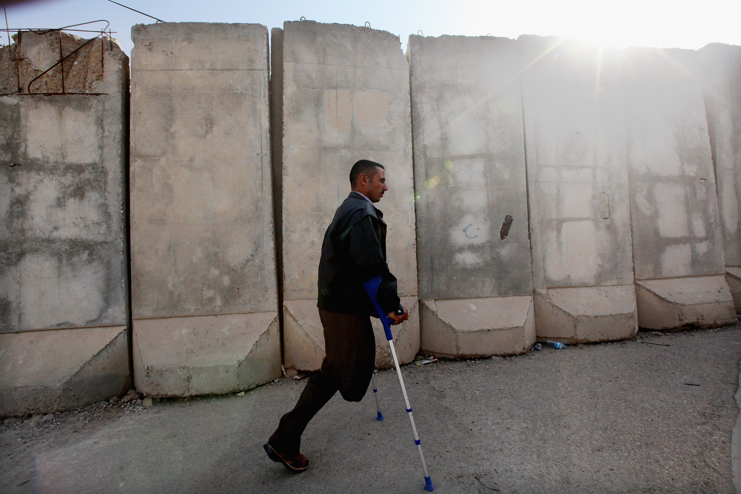 BAGHDAD, IRAQ - DECEMBER 11: Disabled athlete Saad Hussein, who said he was wounded by an American bomb in January, 2008, walks past a blast wall through the Al Thura Disabled Veteran’s Community to meet a family member who lives there on December 11, 2011 in Baghdad, Iraq. Hussein said he was farming with his cousin when the bomb struck. Iraq is transitioning nearly nine years after the 2003 U.S. invasion and subsequent occupation. American forces are now in the midst of the final stage of withdrawal from the war-torn country. At least 4,485 U.S. military personnel have died in service in Iraq. According to the Iraq Body Count, more than 100,000 Iraqi civilians have died from war-related violence. (Photo by Mario Tama/Getty Images)
