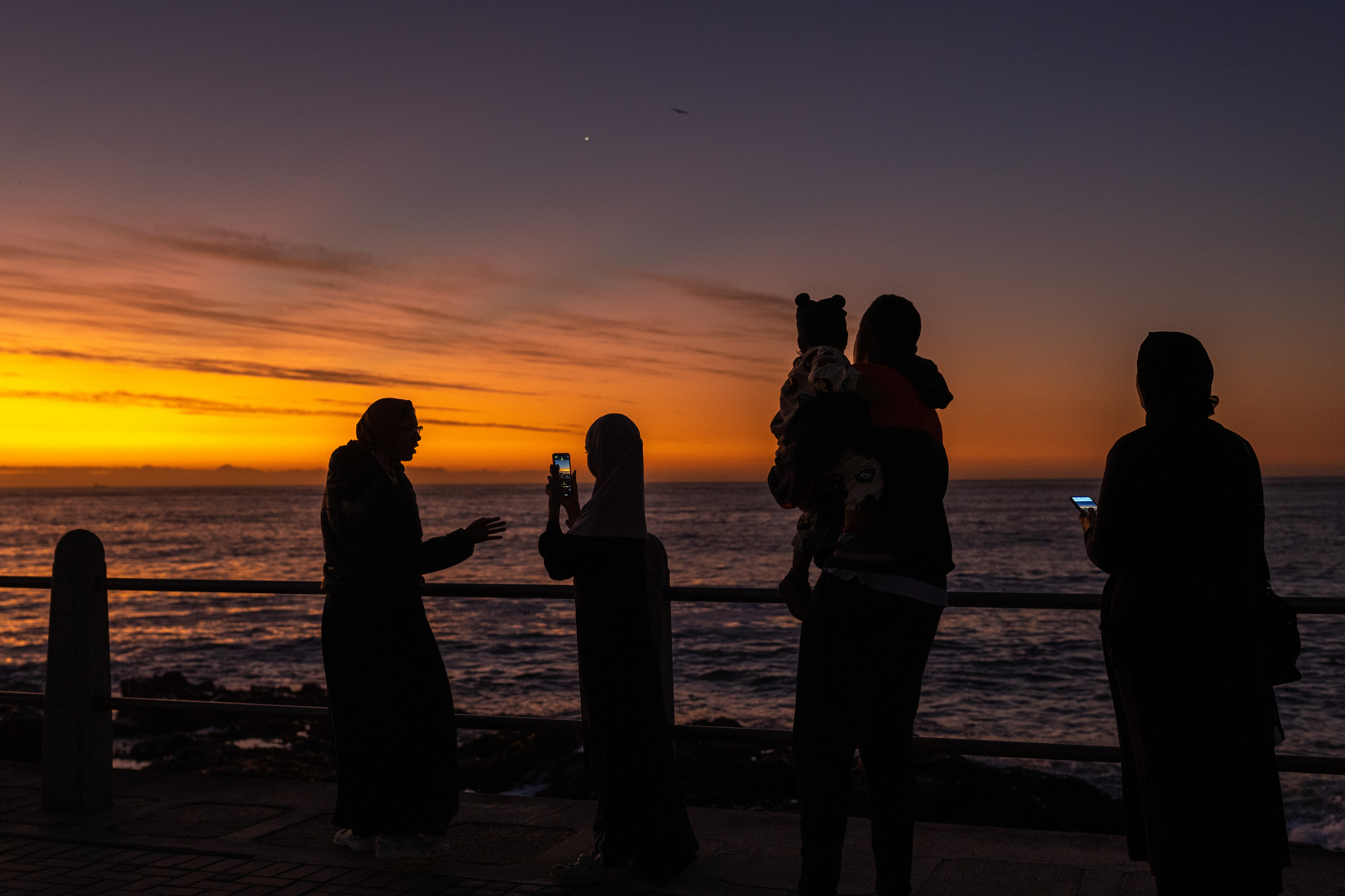 A photo of people standing in front of the sea, watching the sunset.