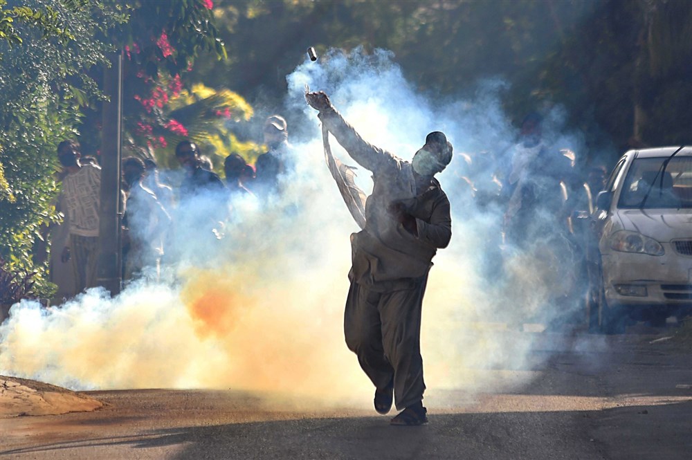 A supporter of former Prime Minister Imran Khan throws a tear gas canister back during clashes with security forces in Karachi, Pakistan
