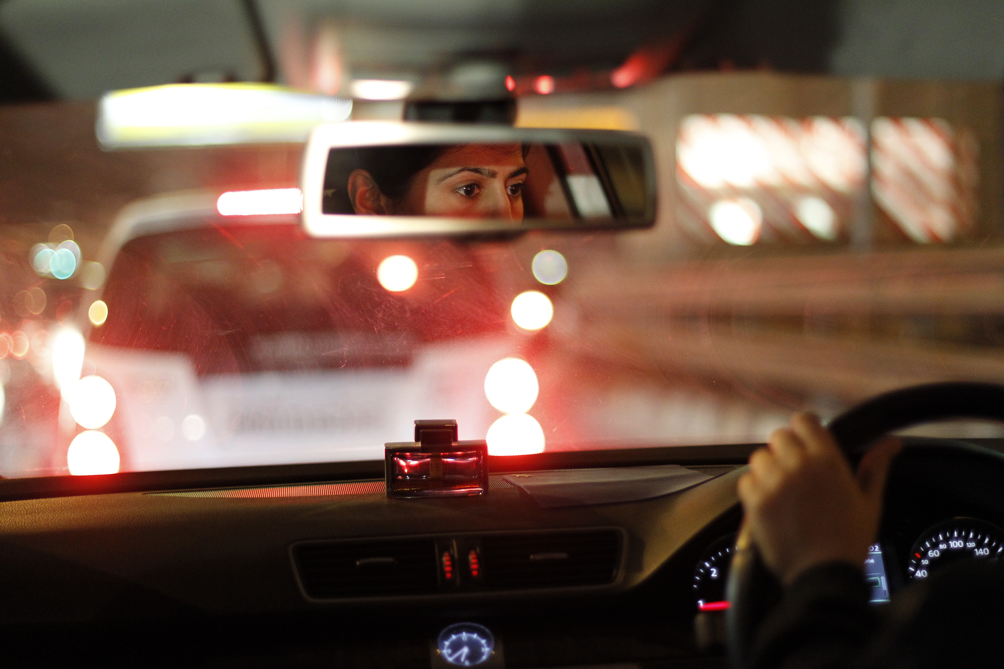 A woman's face can be seen in a car's rear-view mirror