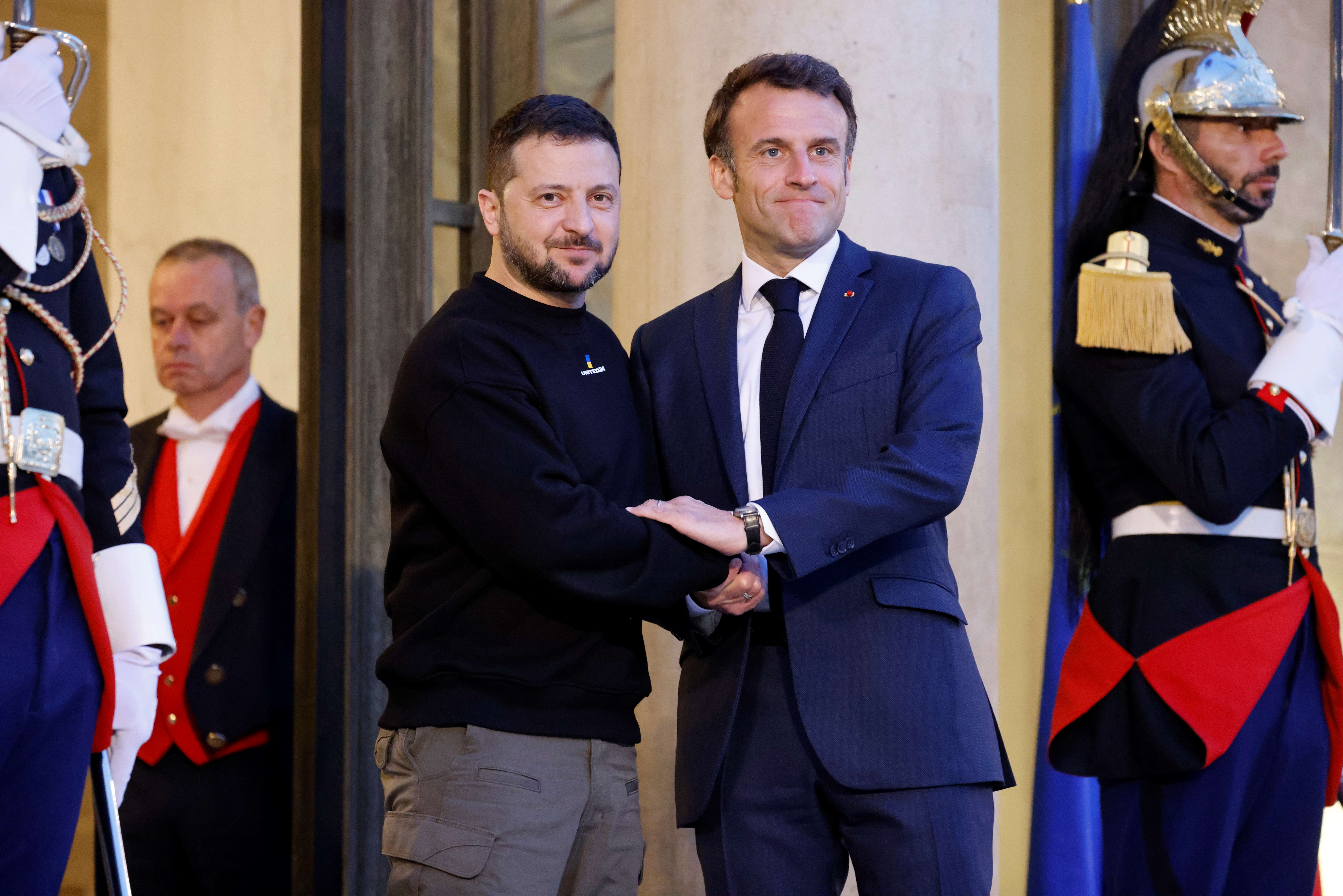 French President Emmanuel Macron greets Ukrainian President Volodymyr Zelenskyy at the Elysee Palace in Paris, France. Macron is in a blue suit and tie, while Zelenksyy is in a black sweat shirt and khaki trousers. They look resolute. 