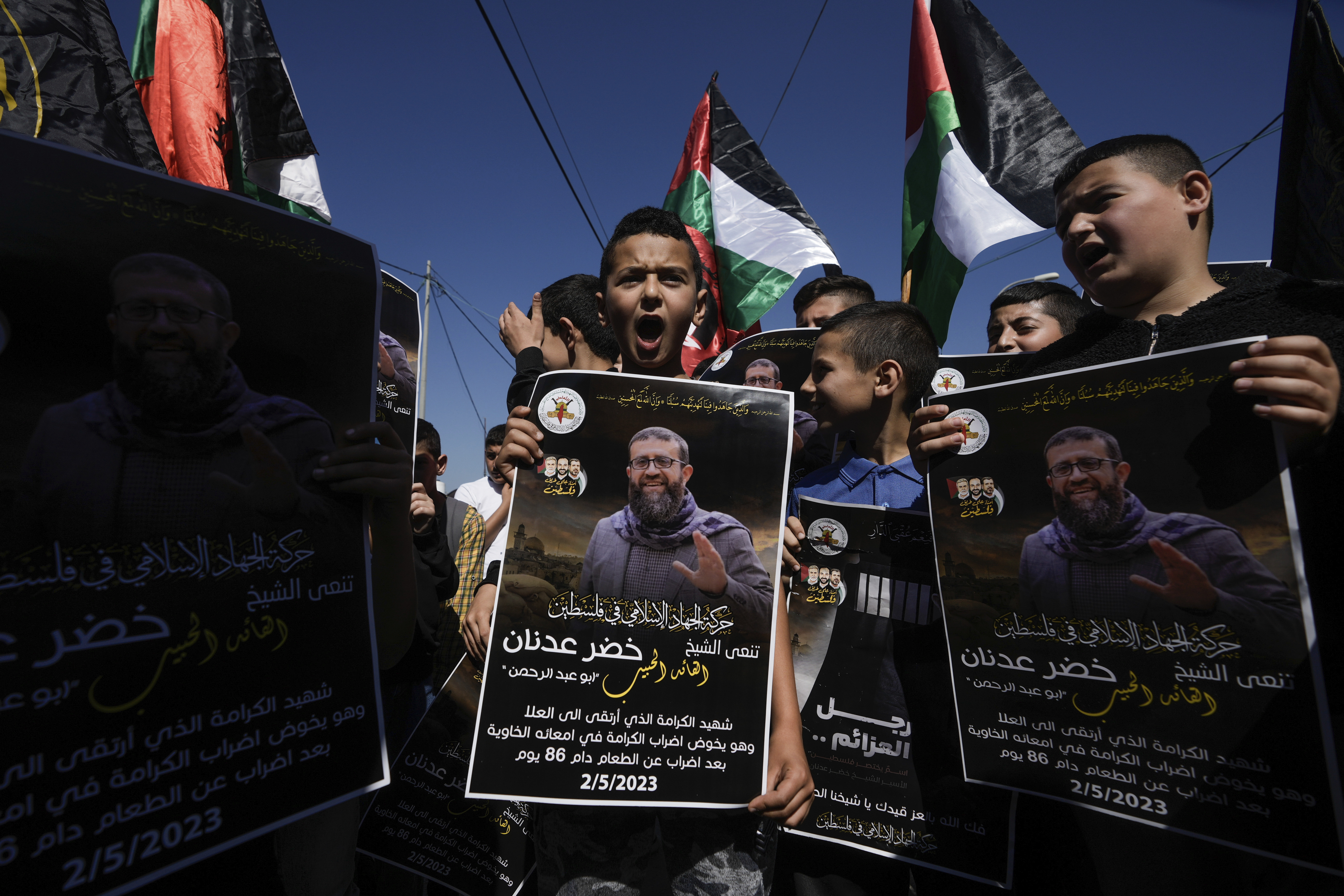 Palestinian kids wave their national flag and hold posters showing Khader Adnan