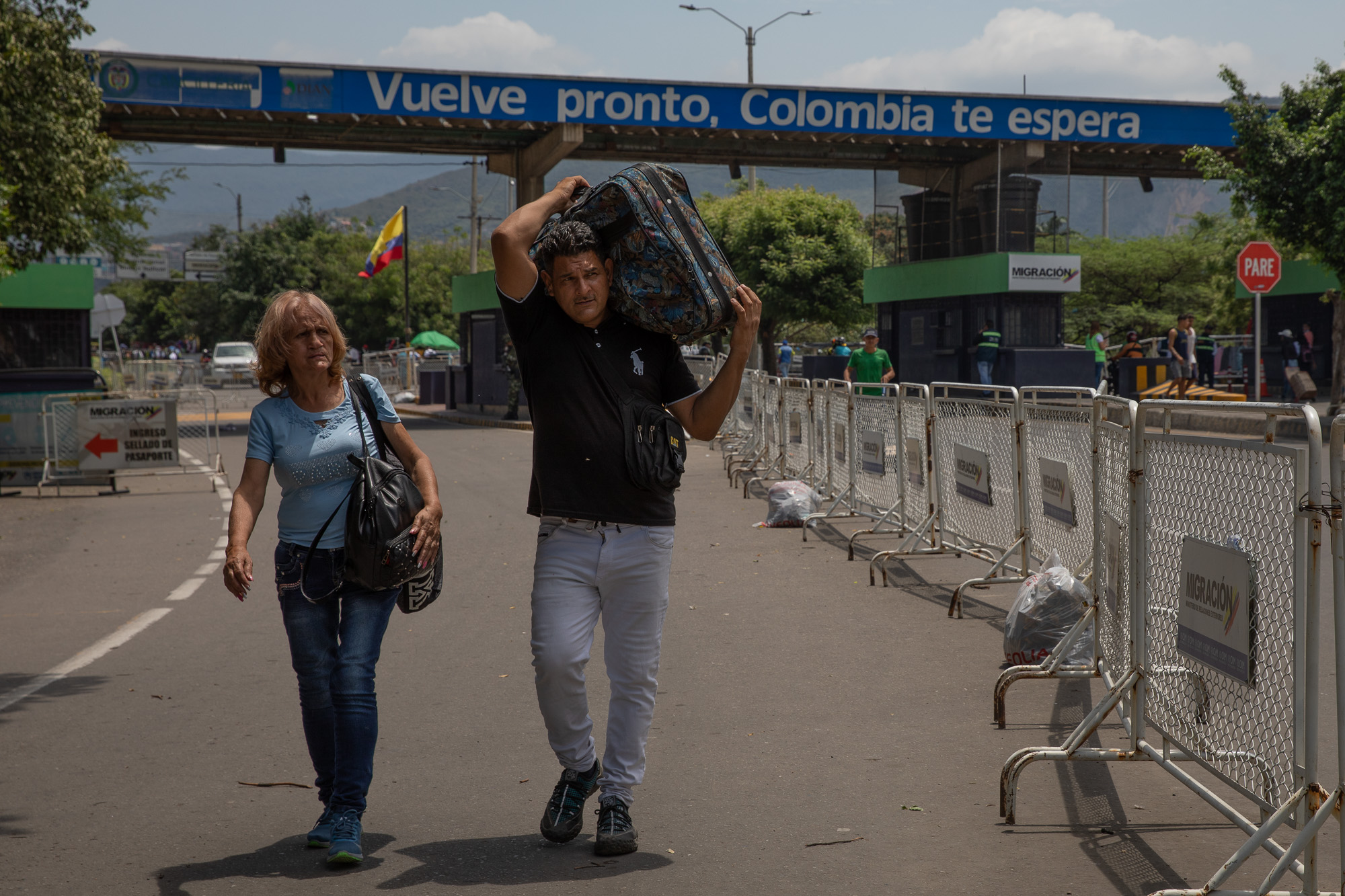 A woman with a backpack and a man walk side by side on a road, with the latter carrying a suitcase over his shoulder.