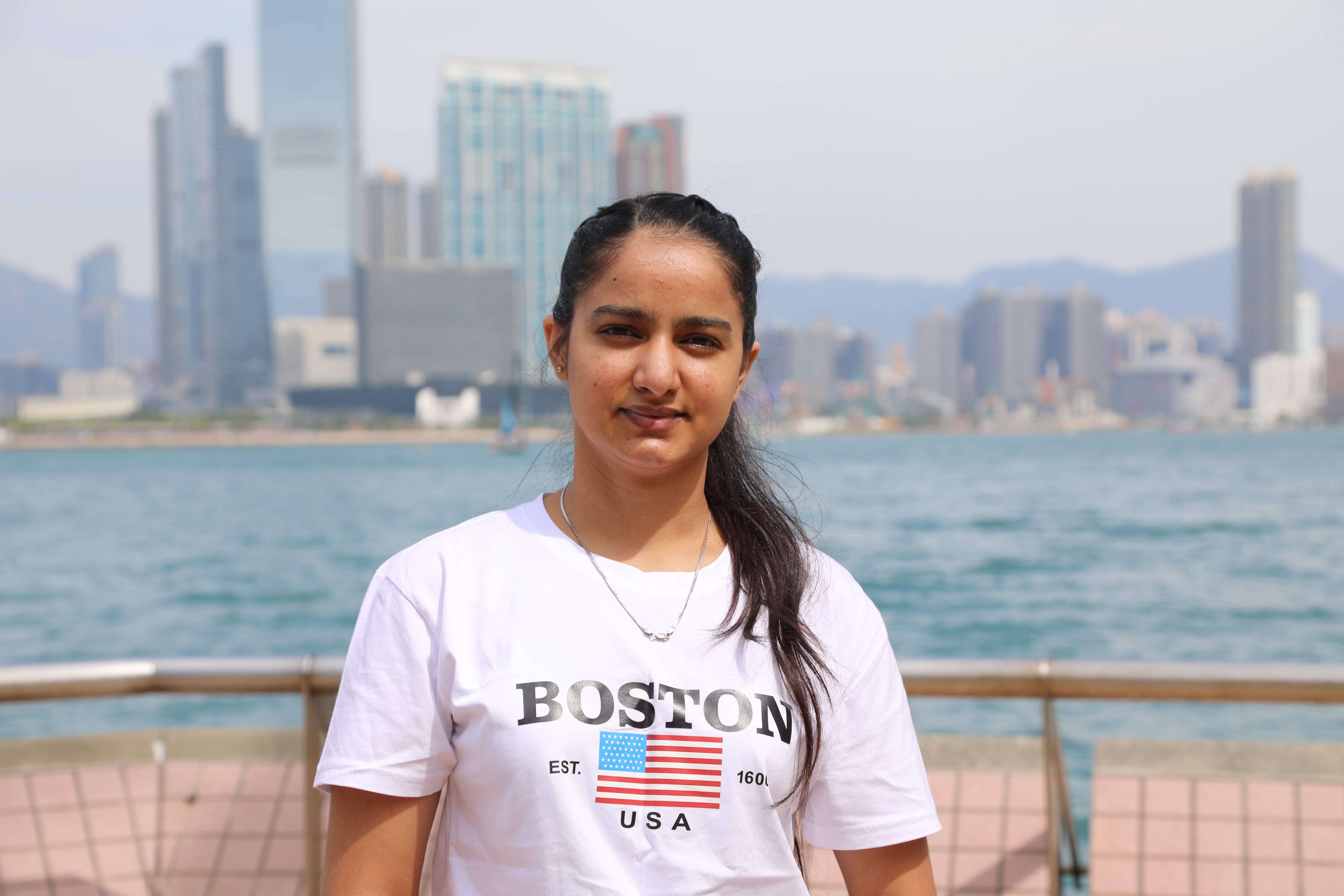 A portrait of Hardeep. She is standing by the harbour and looks relaxed.