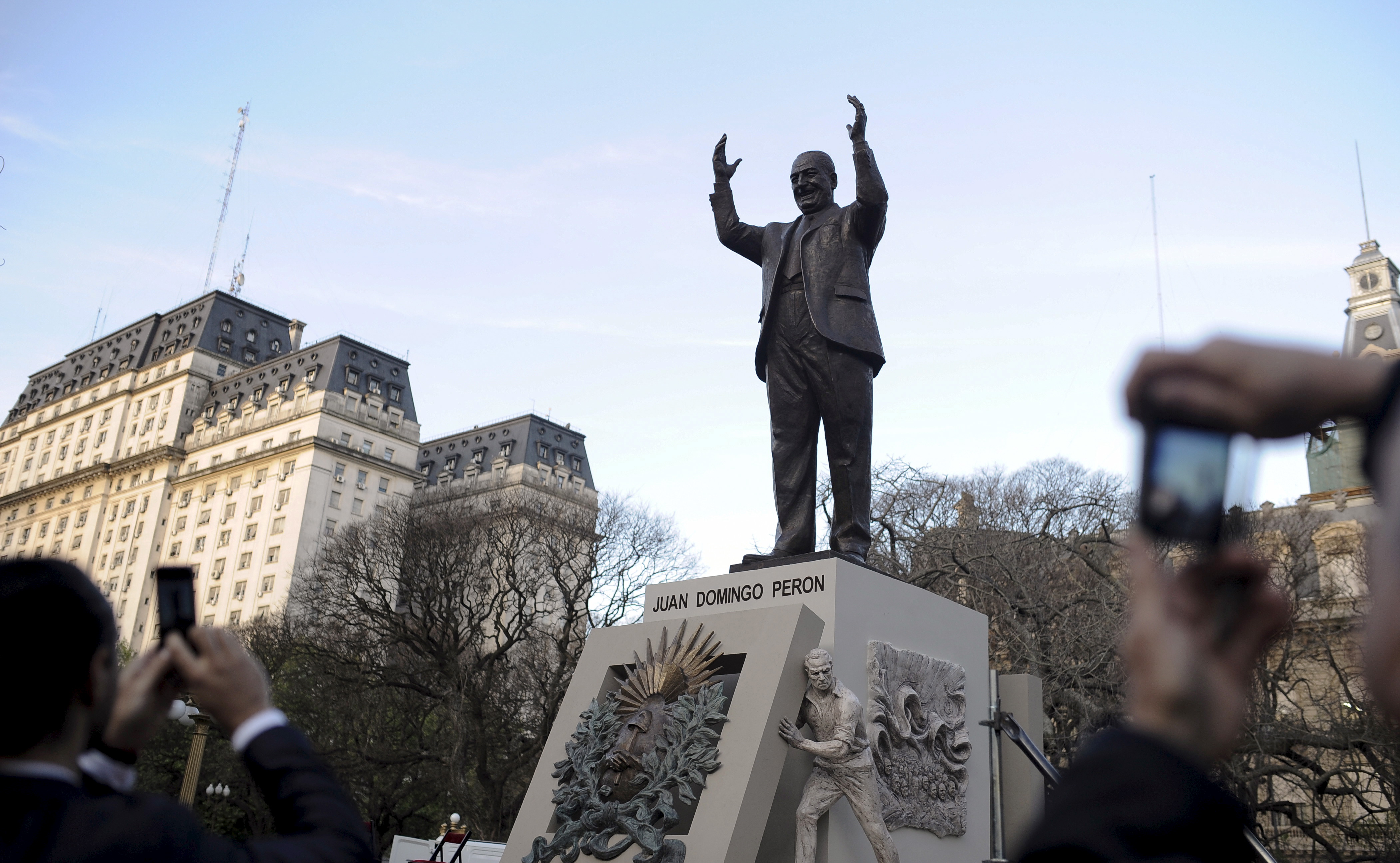 A bronze statue of a man with his arms raised sits in a city square