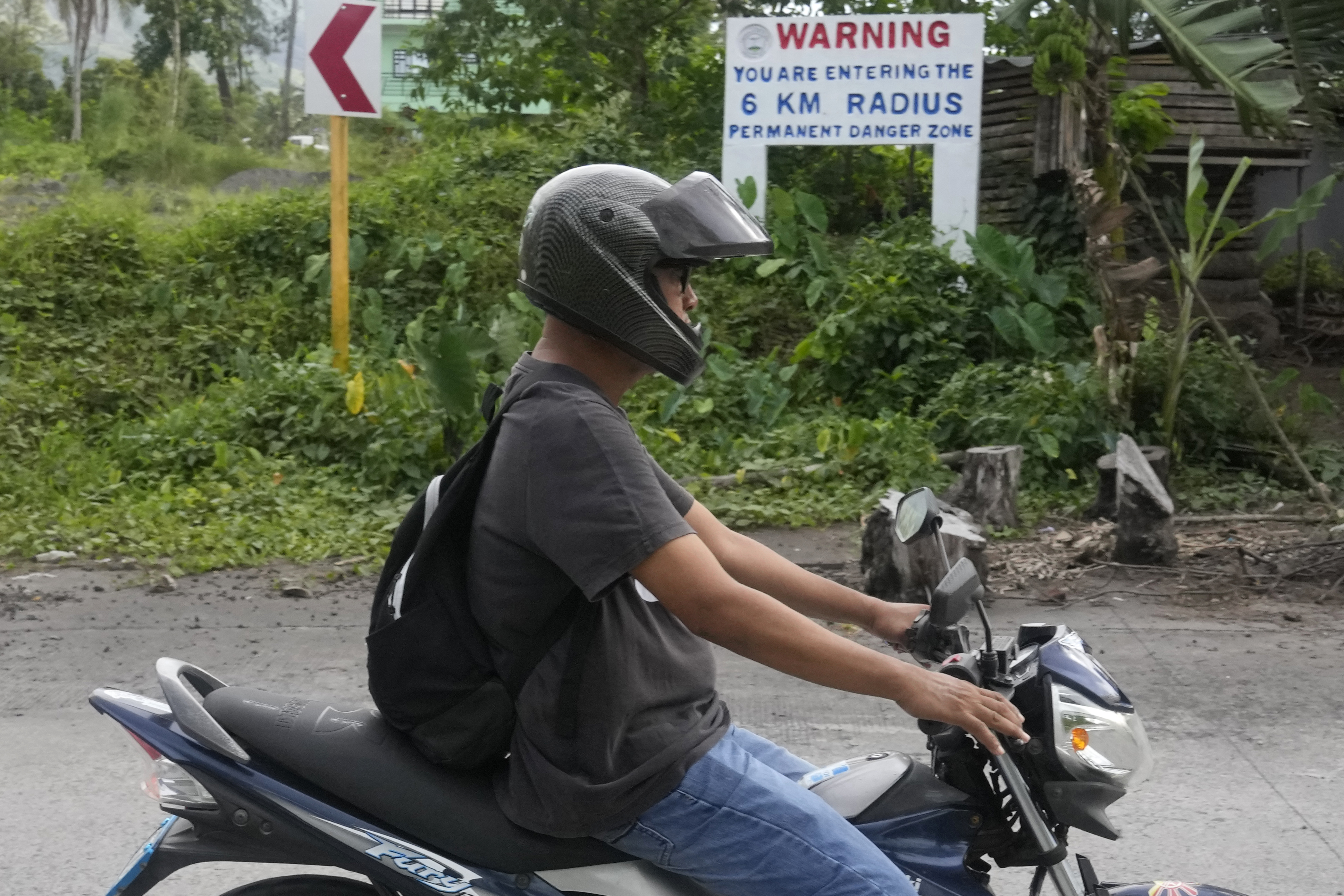 A man passes by a warning sign along a road in Mabinit, located near Mayon volcano