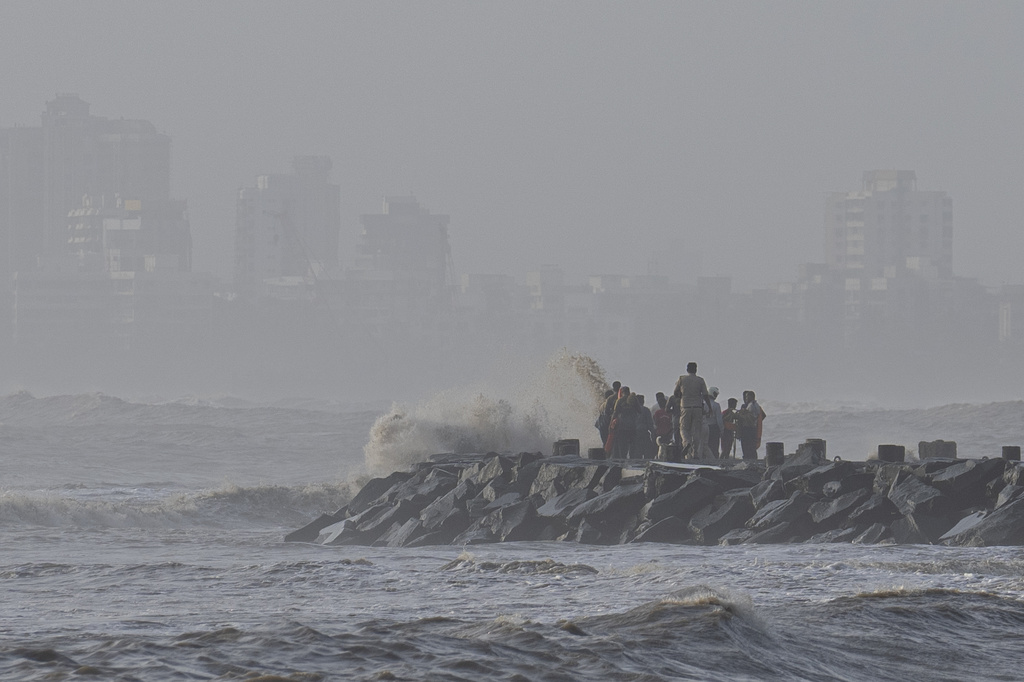 A police officer tries to move people away as high tide waves hit the Arabian Sea coast in India