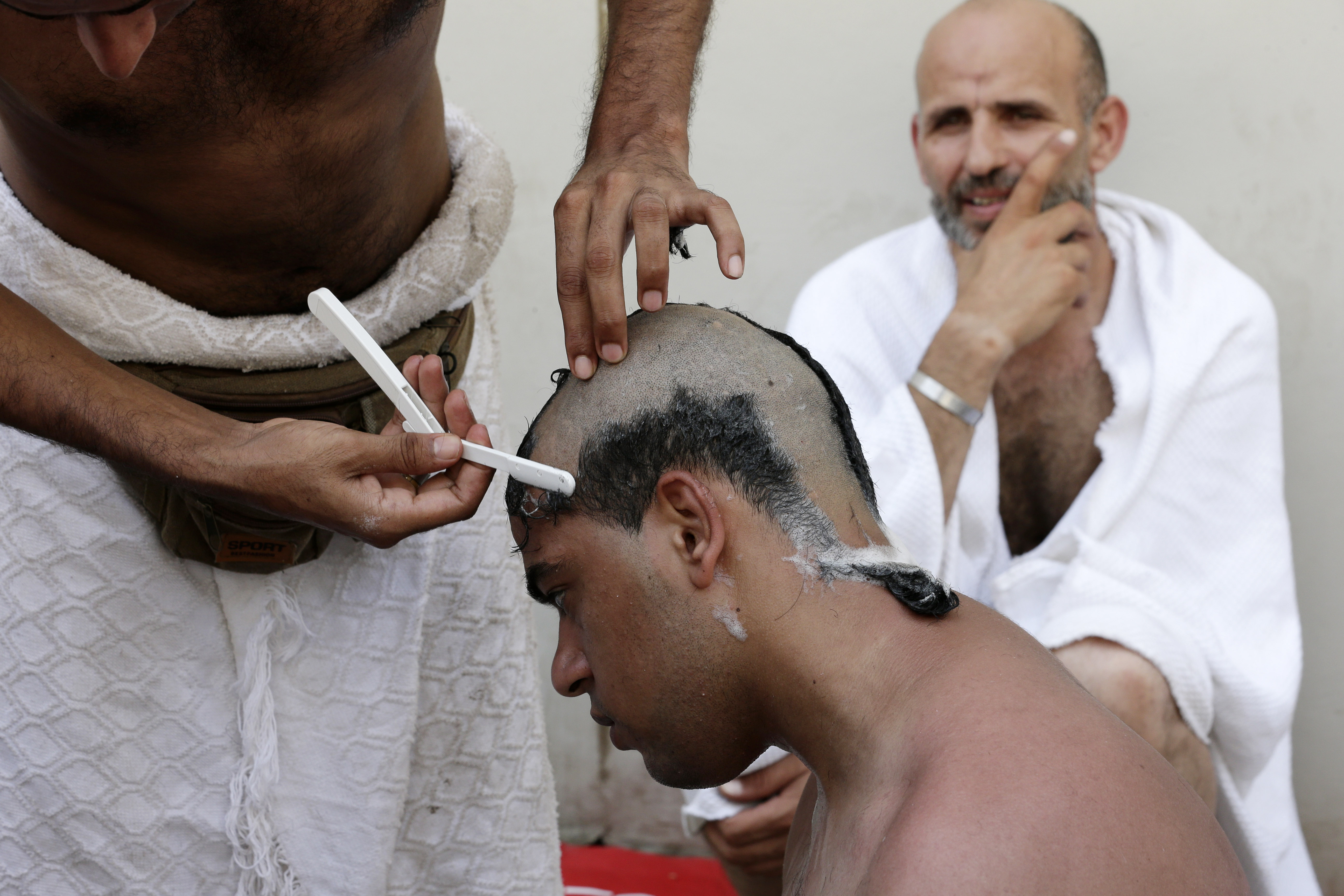 A Muslim pilgrim has his head shaved by another pilgrim holding a straigh razor