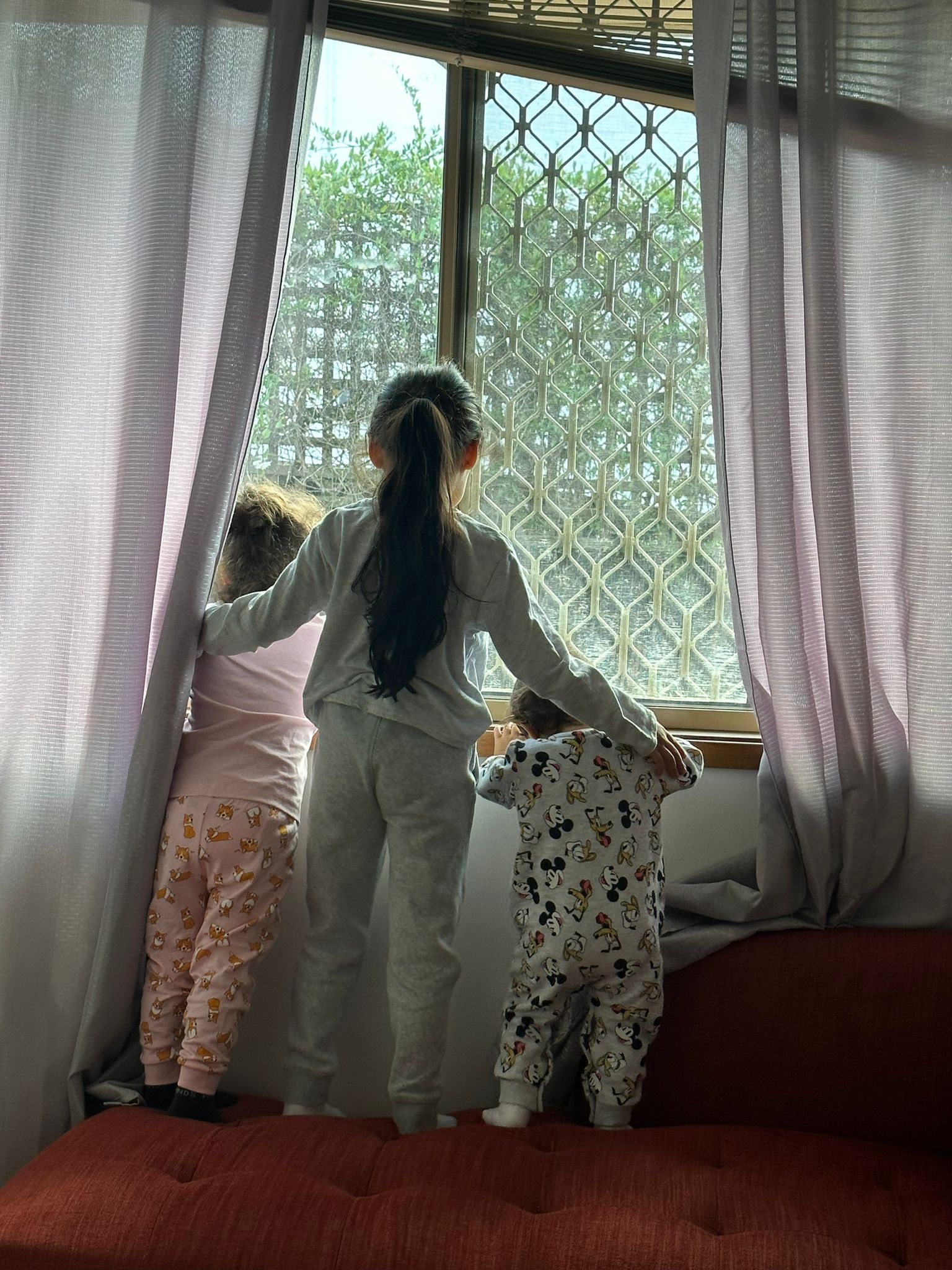 Children looking out of a window. They have their backs to the camera