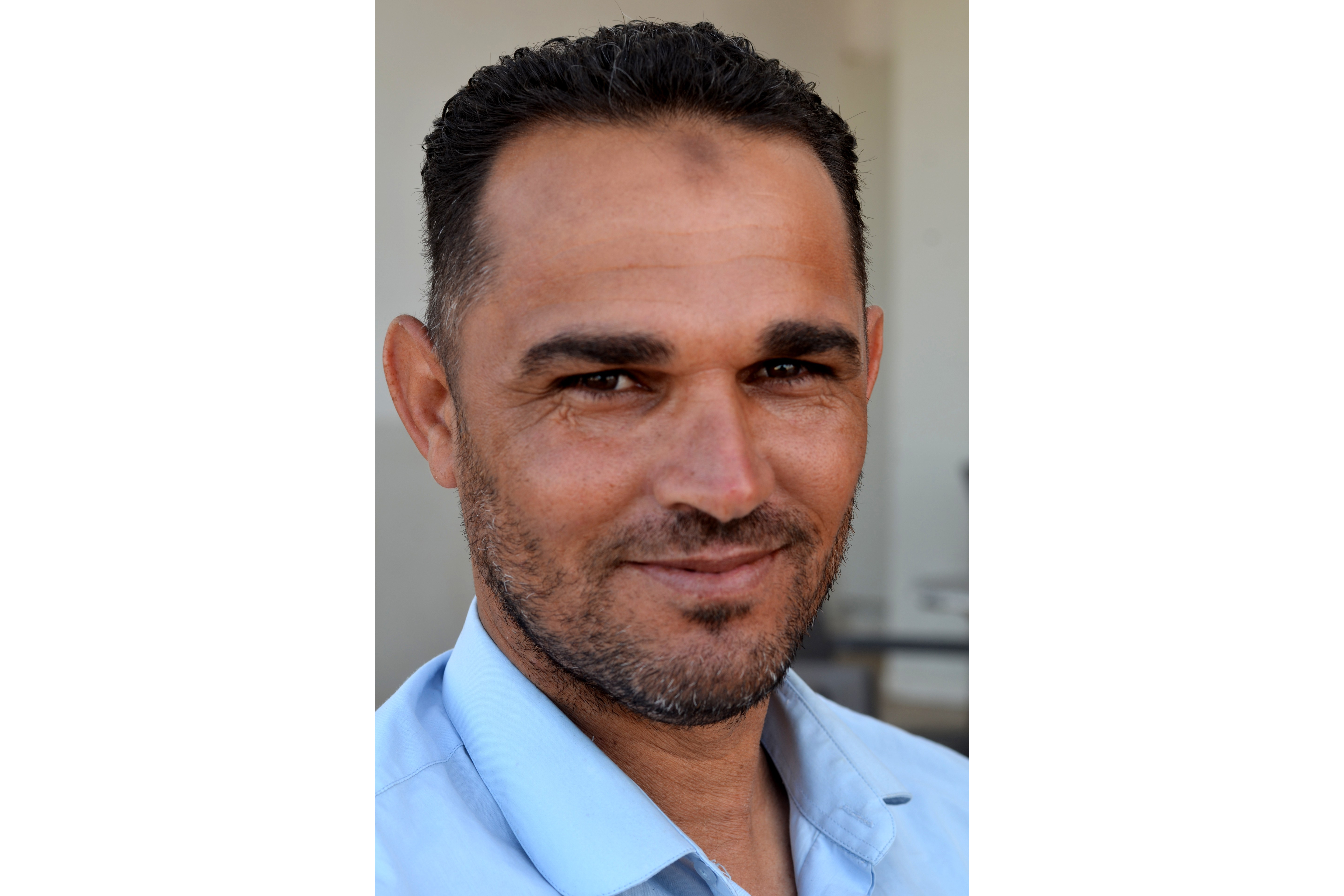 Sassi Alaya smiles at the camera, wearing a blue button shirt