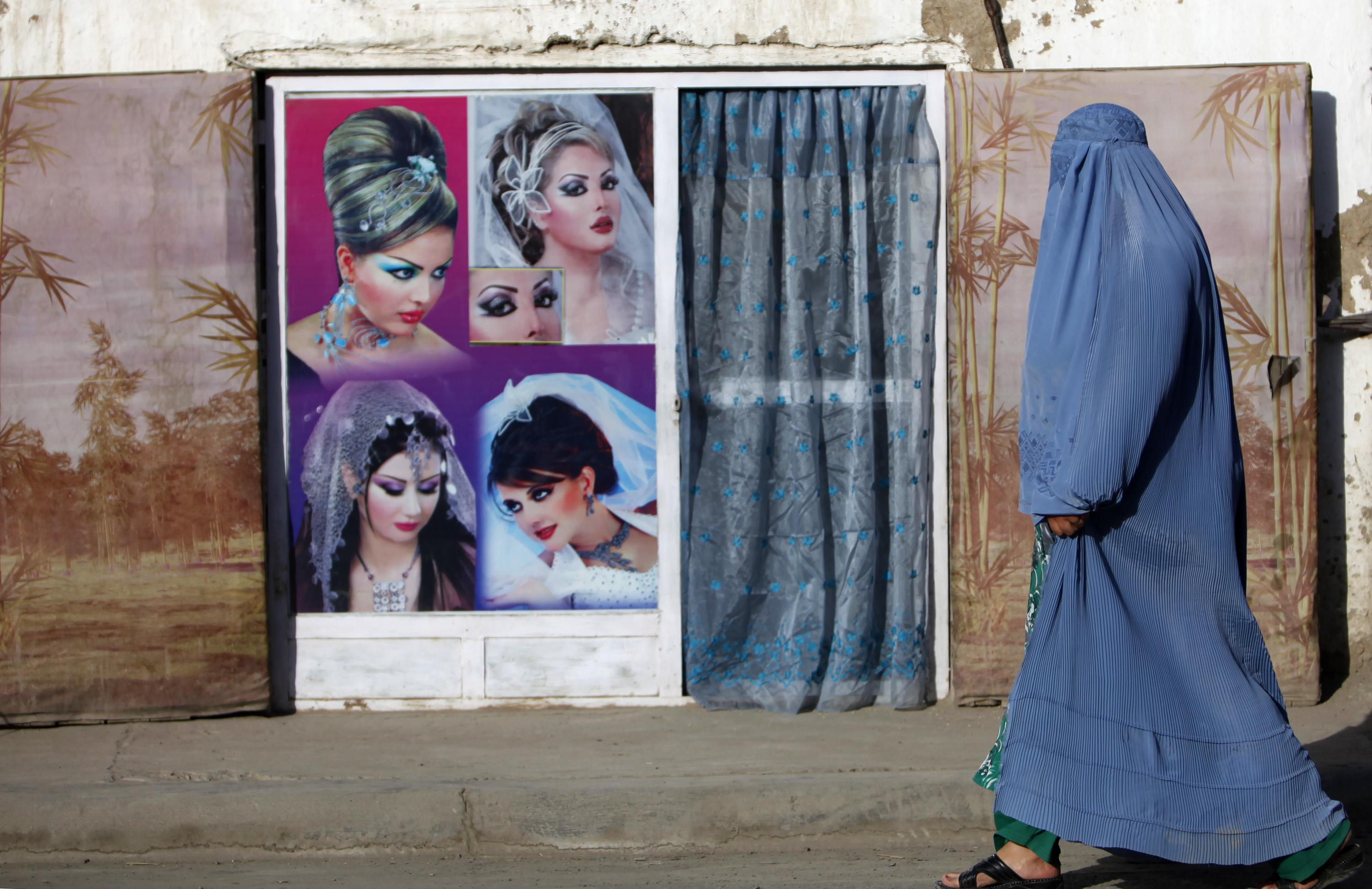 An Afghan woman in a burqa walks past a beauty saloon shop in Kabul