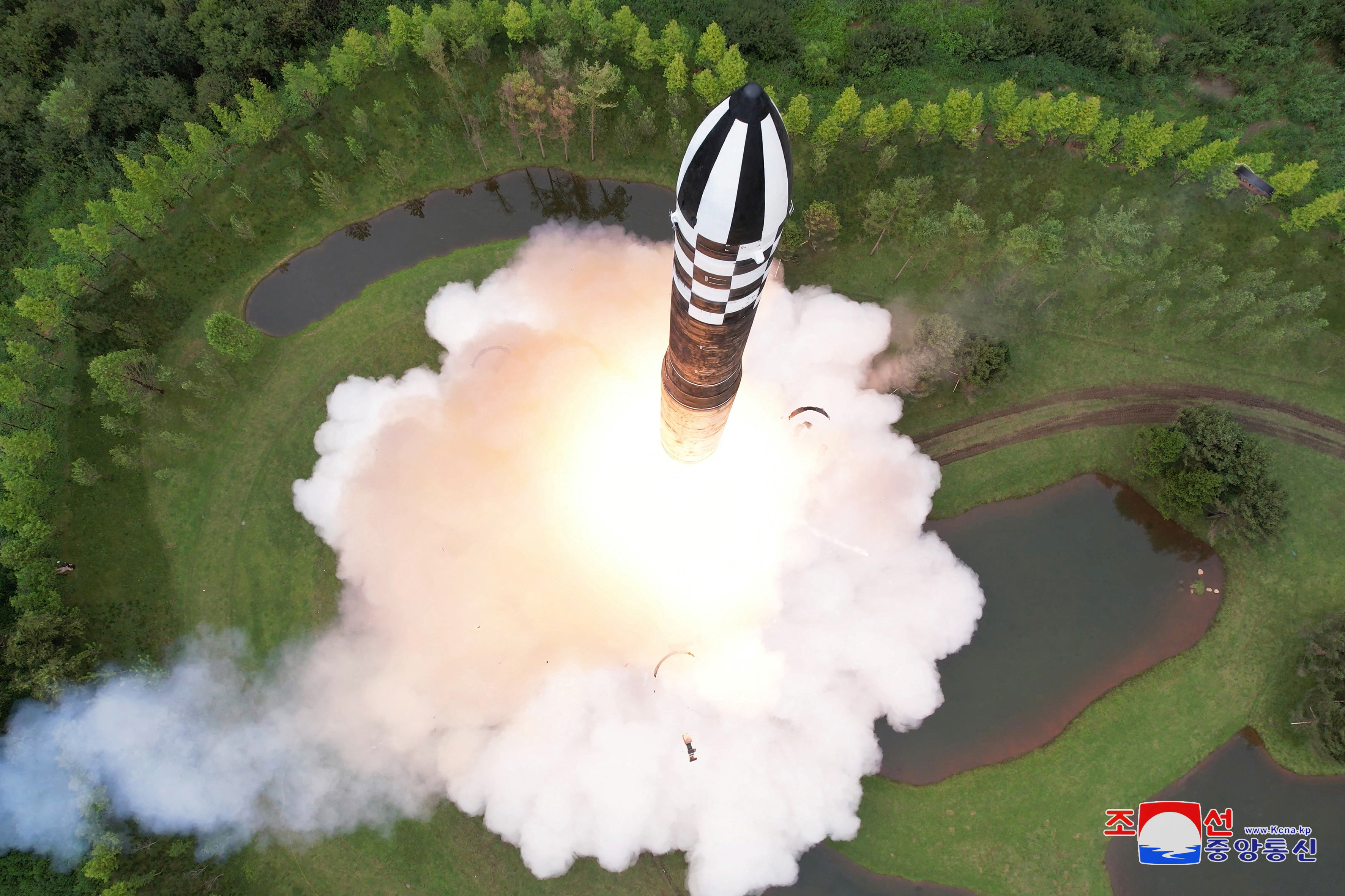 A view of the black and white striped nose cone with clouds of smoke below, as well as trees.