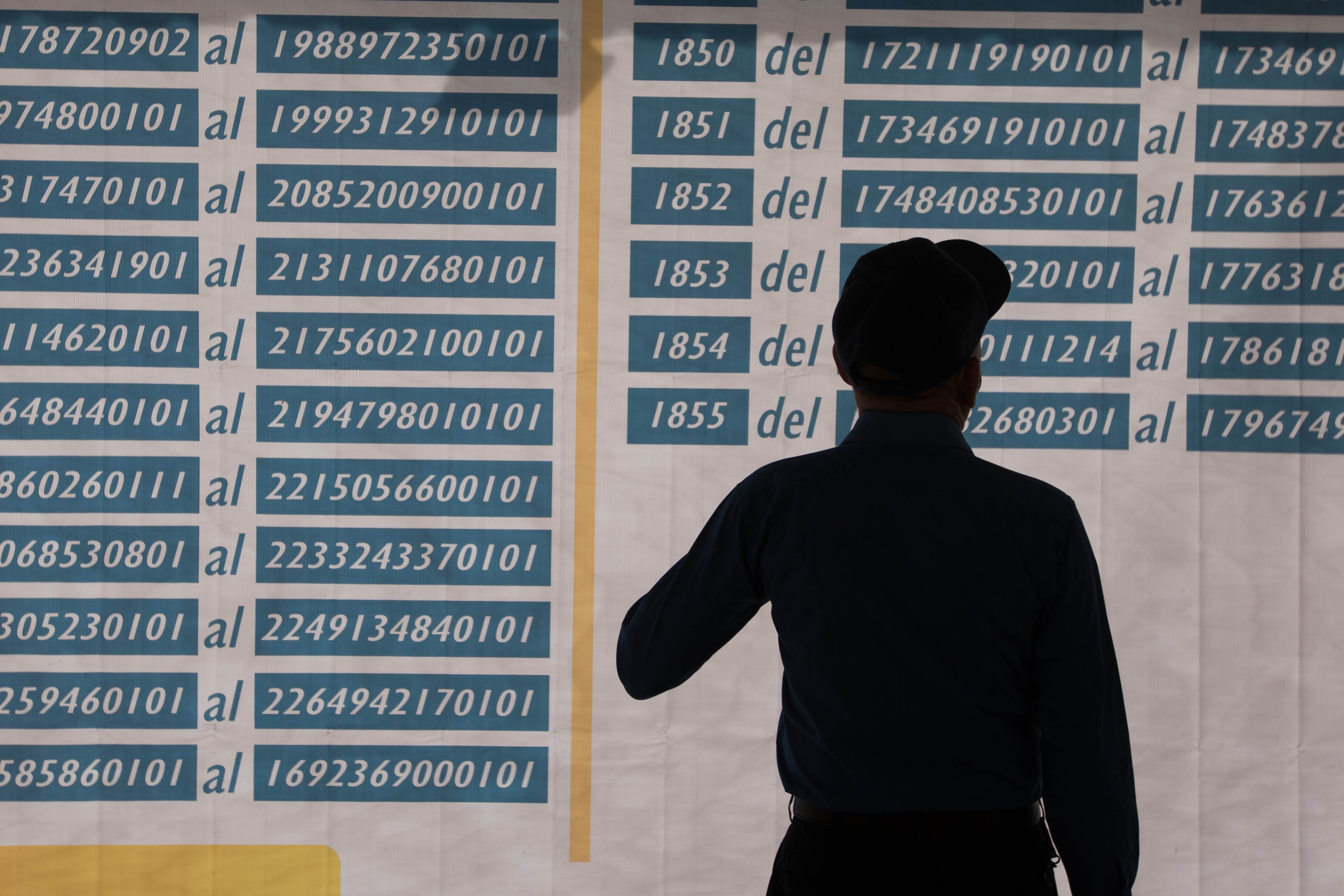A man in silhouette checks a white board with blue numbers, indicating polling sites.