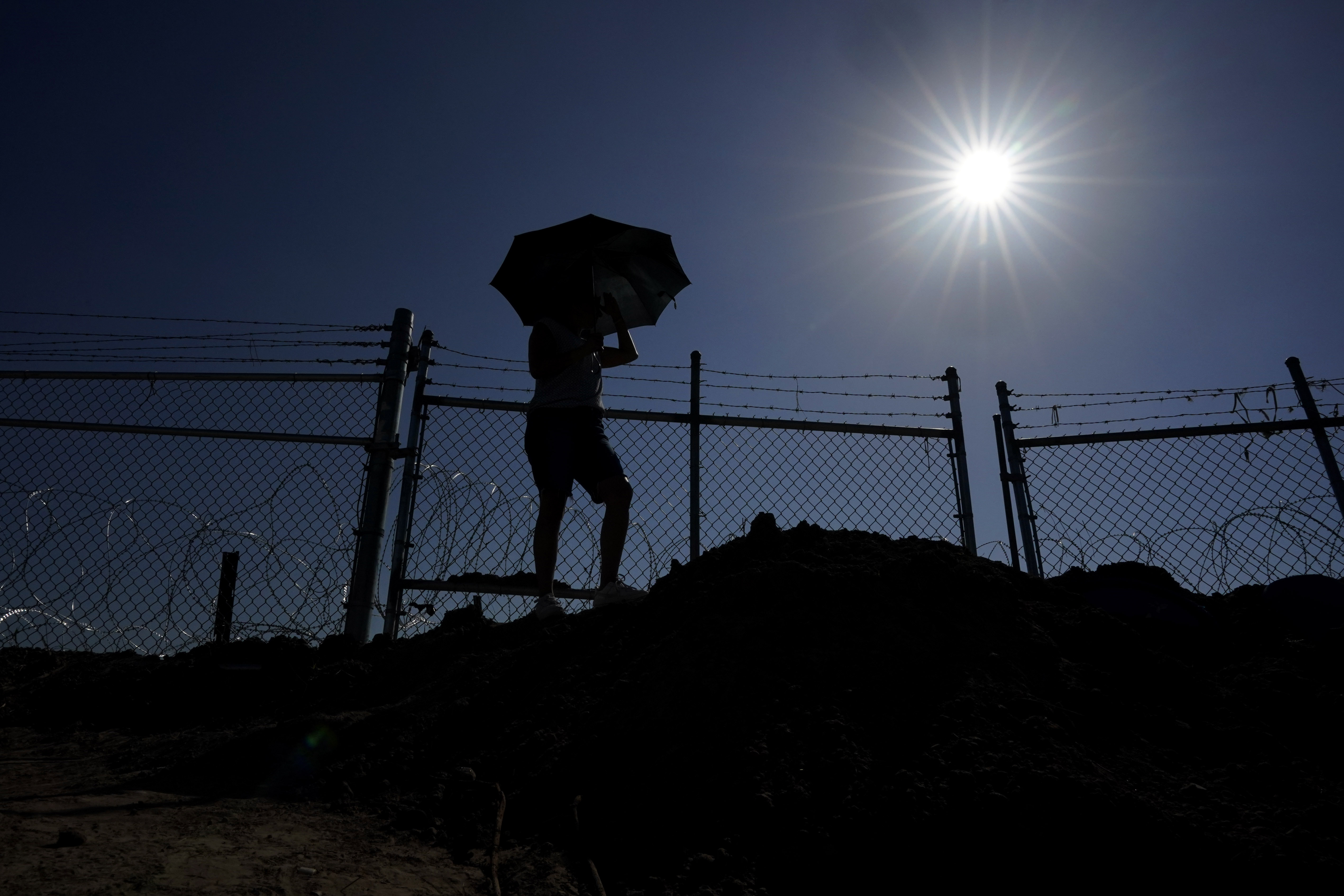 Magali Urbina shields herself from the sun with an umbrella as she watches as the state installs large buoys