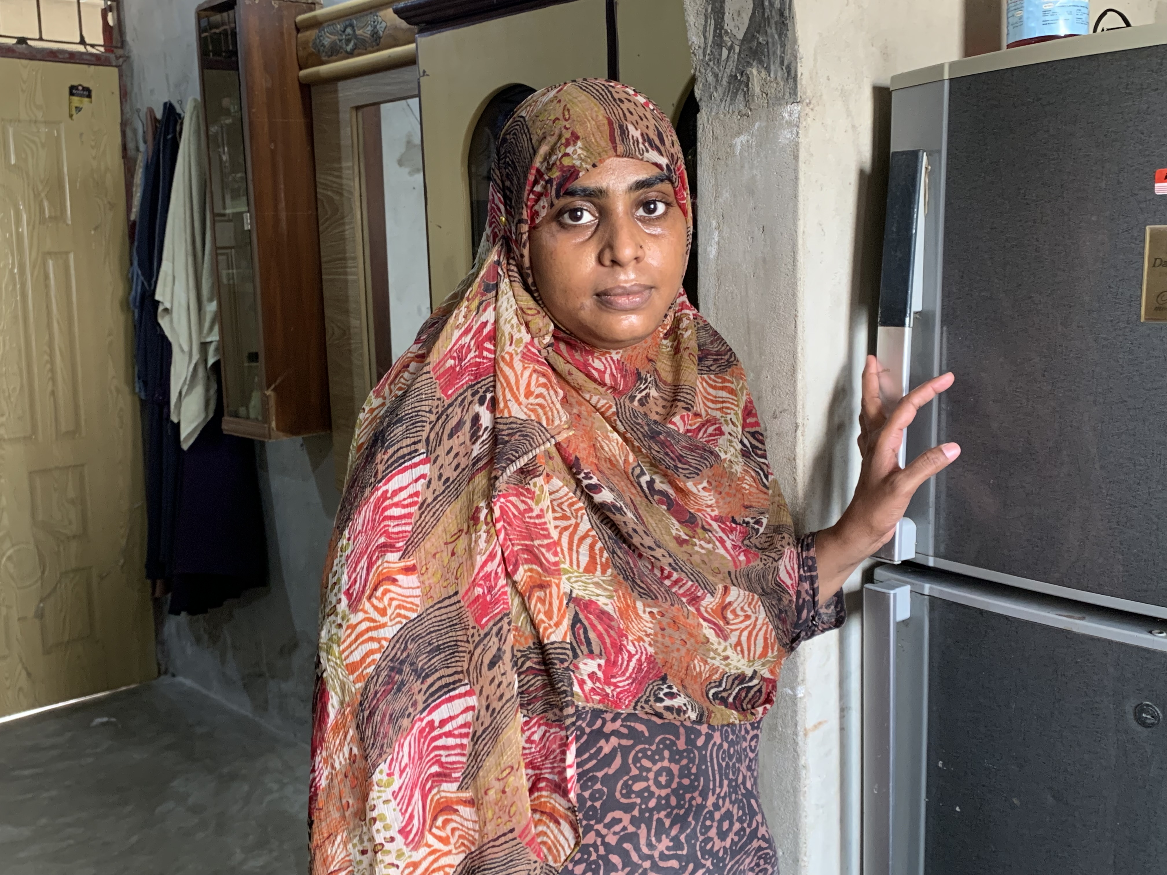 A photo of Aisha with her hand on the fridge next to her.